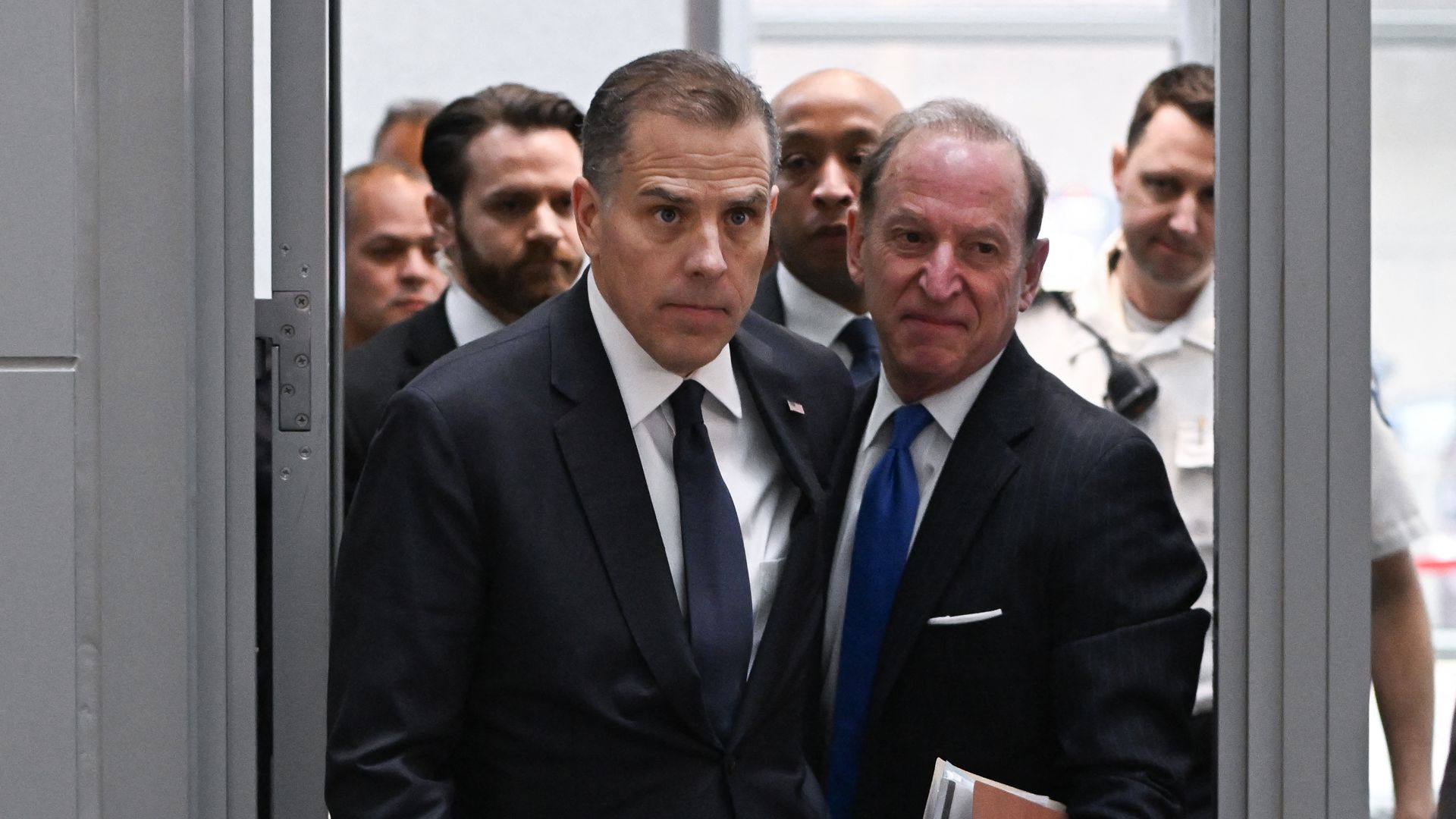 Hunter Biden and others walk through a door. Most are dressed in suits. 