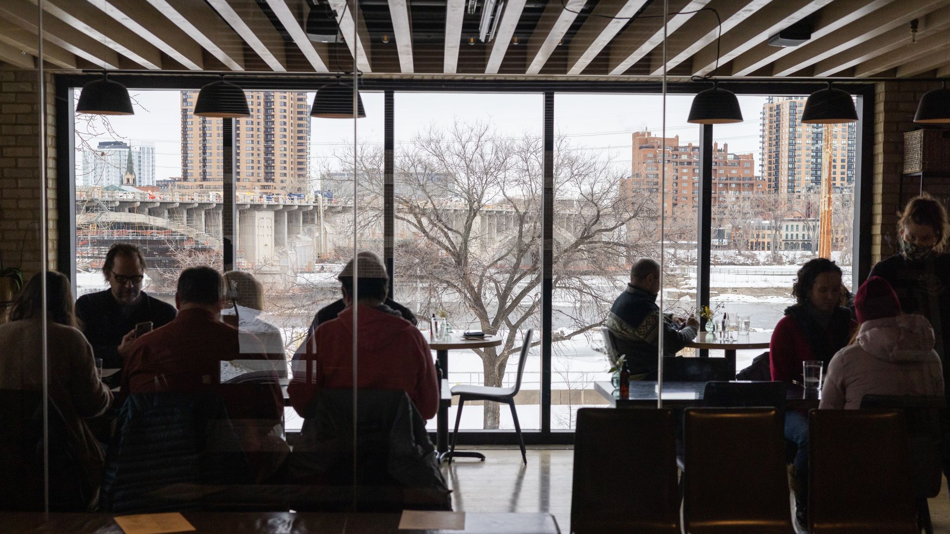 diners in a restaurant with a large window showingthe mississippi river and stone arch bridge in the background.