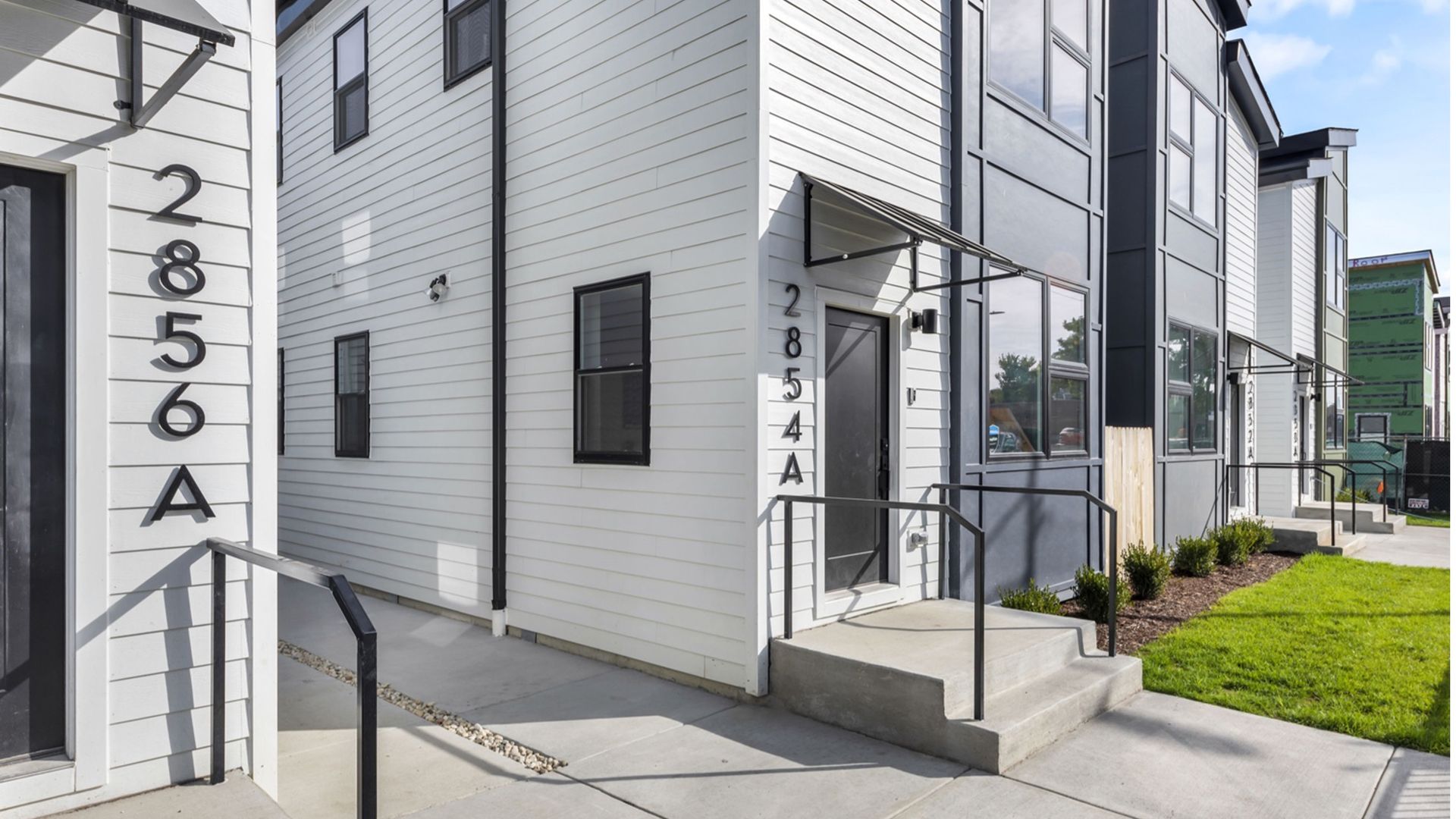 Modular white-and-gray townhomes, with a small patch of grass in the frontyard.