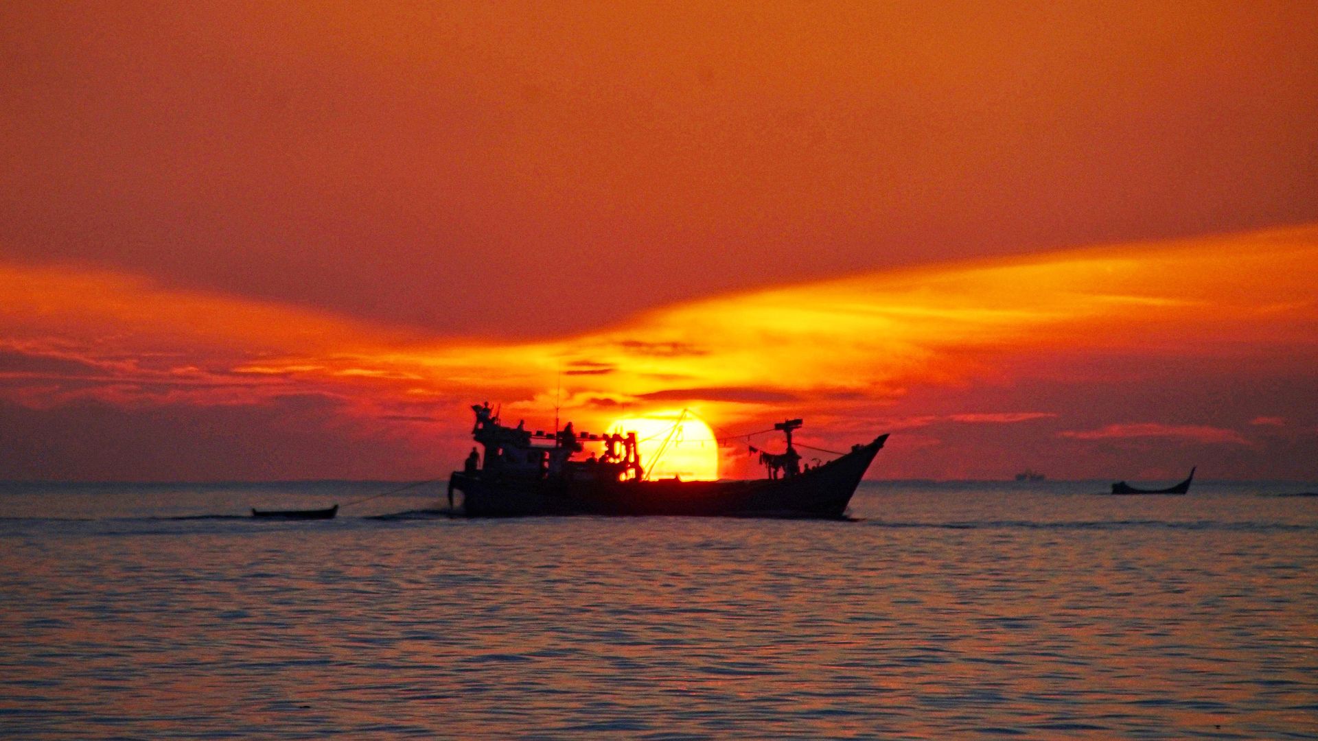 Photo of a fishing boat on the water against the backdrop of a red-orange sunset