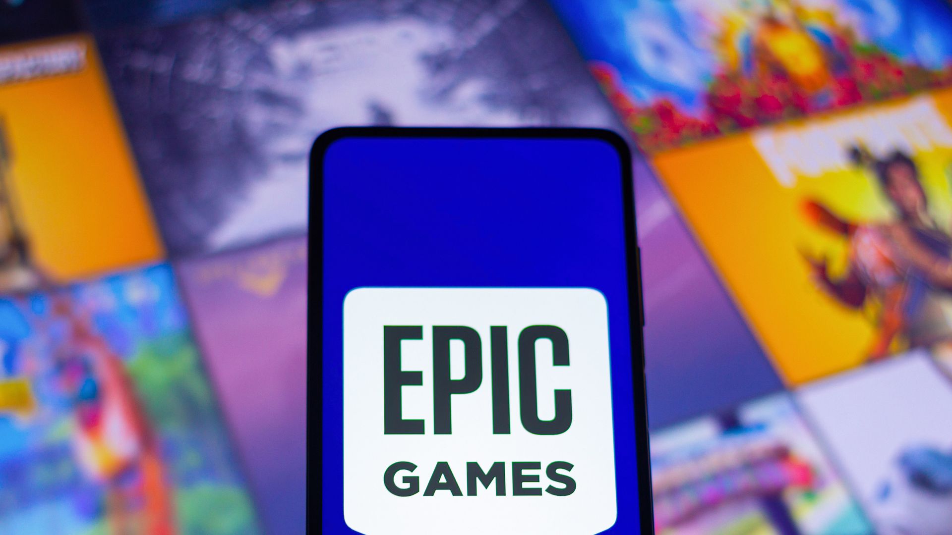 Photo illustration of a phone displaying the Epic Logo, with video game title screens displayed behind the phone