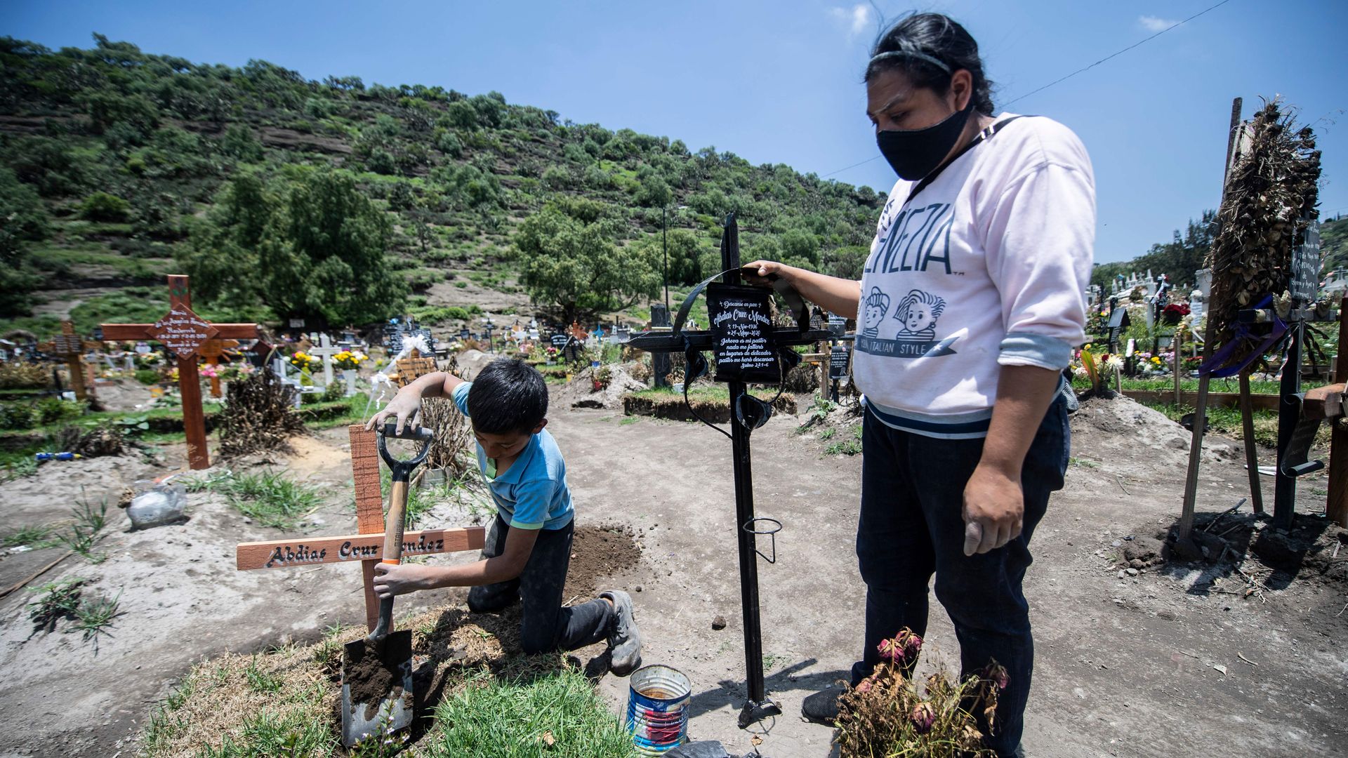 A woman visits two family members who died of COVID-19 while a 10-year-old boy works placing crosses at the San Miguel Xico cemetery on August 5 in Mexico