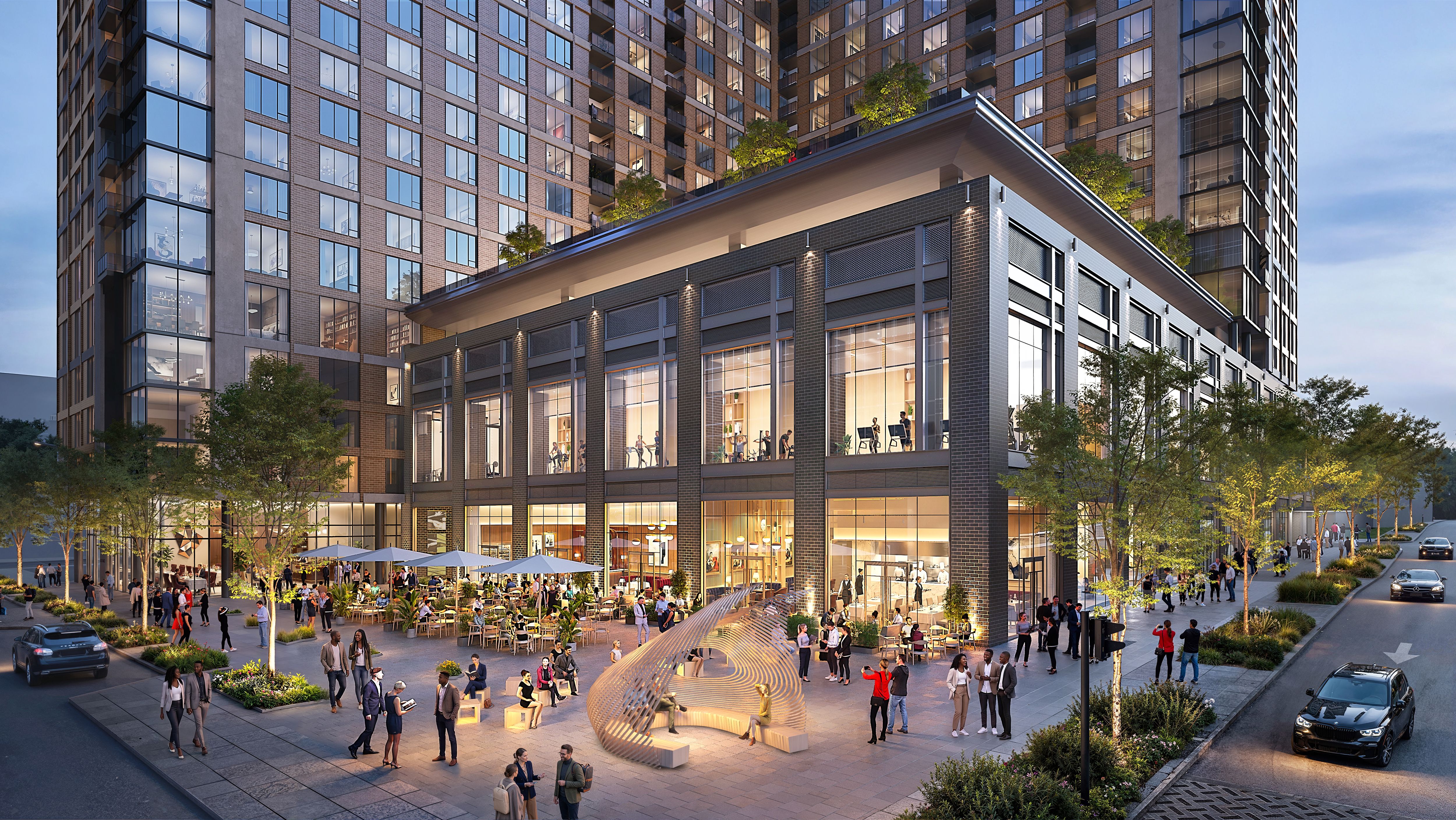 Modern brick high-rise with glass windows and balconies over a busy plaza. People mingle at outdoor cafe seating under umbrellas, with trees and a circular sculptural installation in the foreground.