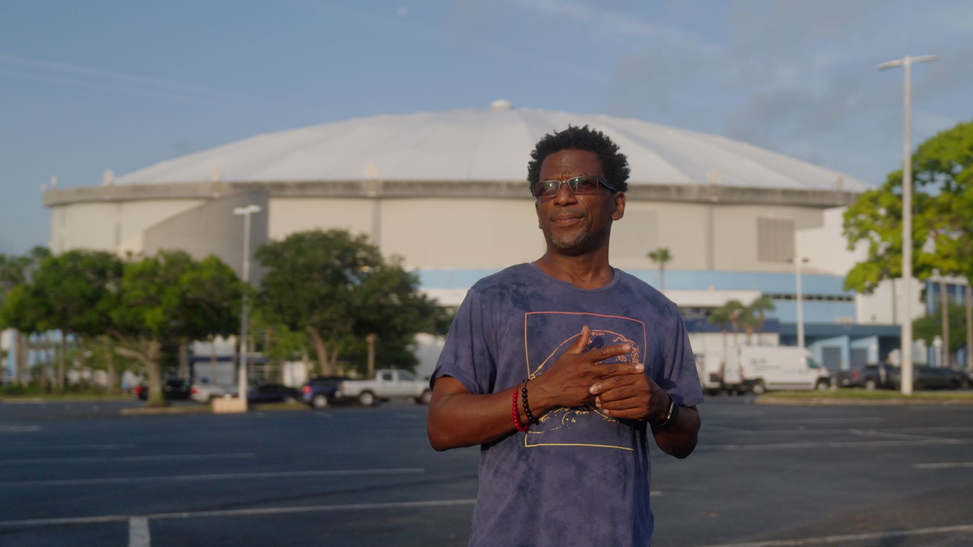 A man in a blue T-shirt looks into the distance while standing in the parking lot with a white dome-shaped in the distance.