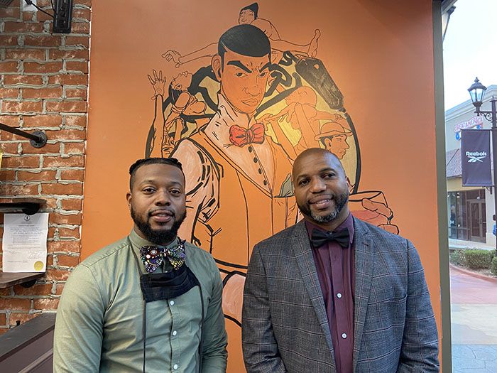 Lead barber Darnele Chisholm and franchise owner Edmund Washington stand in front of a mural in the new No Grease! barbershop.