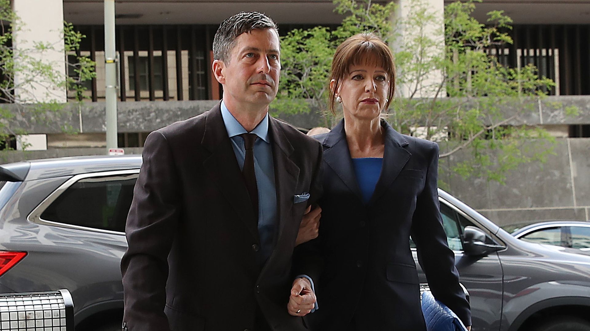 In this image, Sam Patten and his wife walk out of a sedan car with elbows linked. 