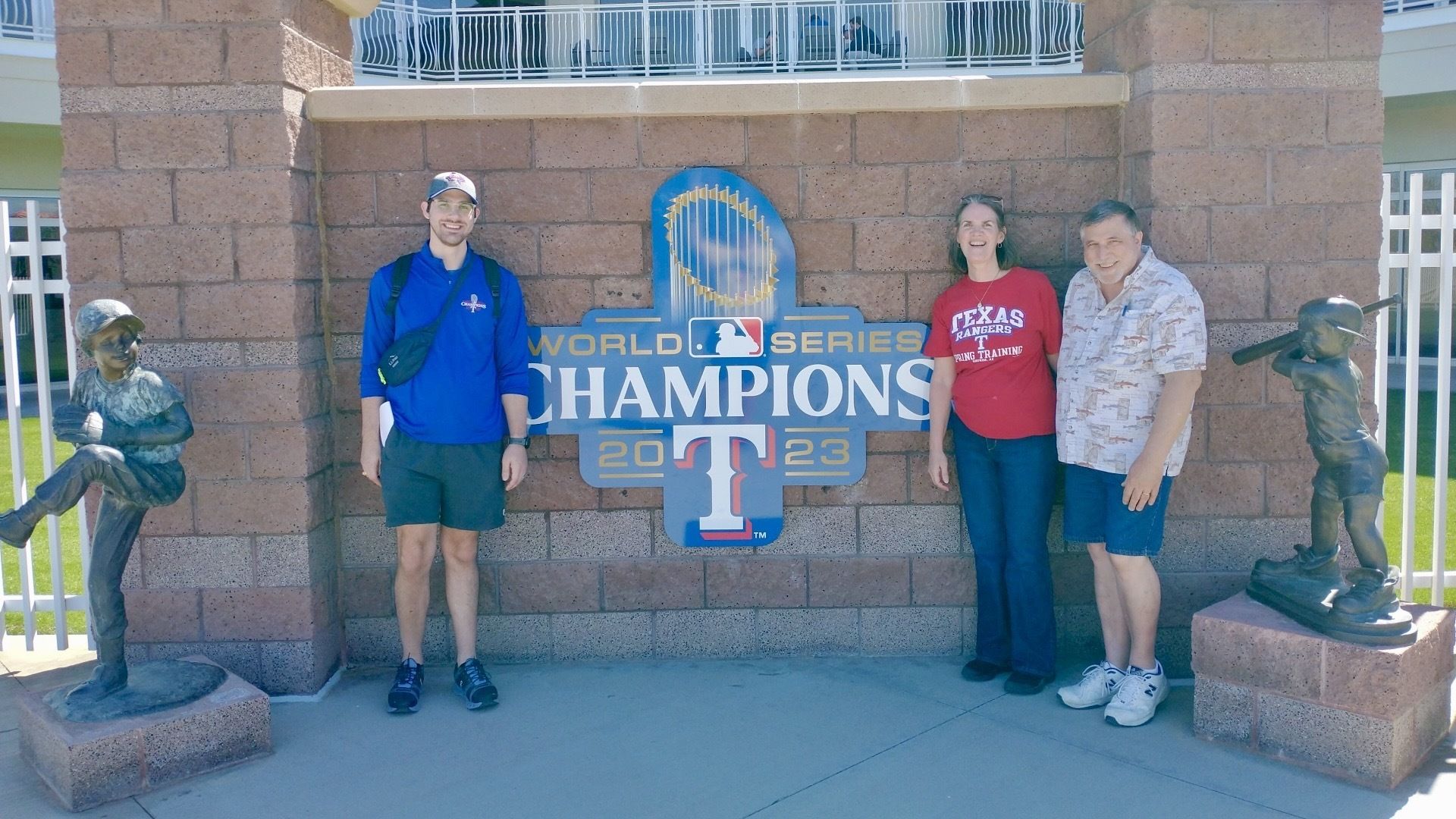 Three people standing in front of a Texas Rangers Champions sign