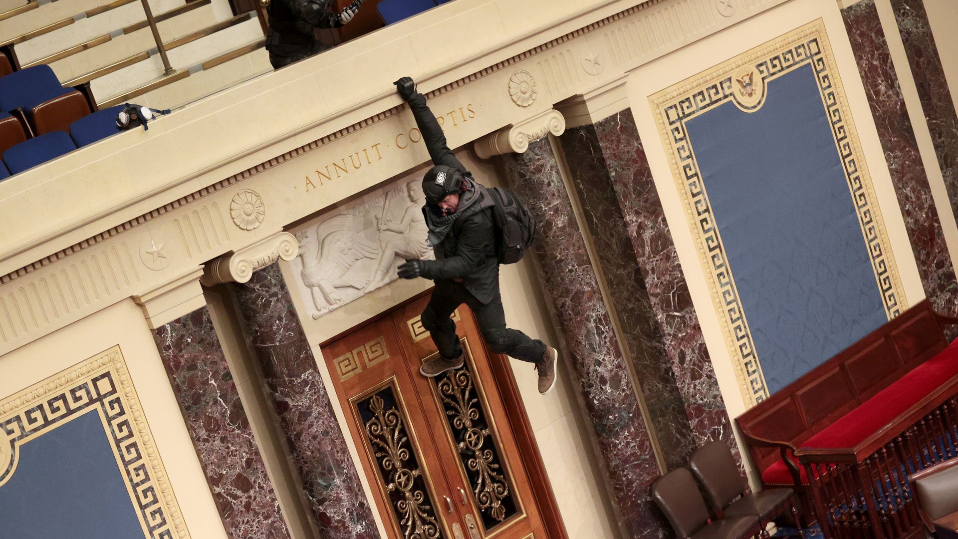 A protestor is seen hanging from the balcony in the U.S. Senate chamber during the Jan. 6 assault.