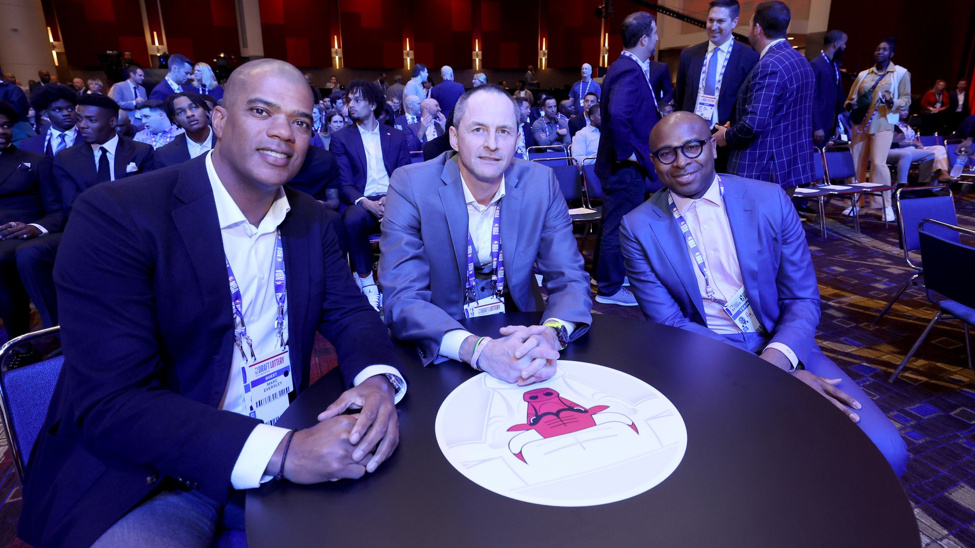 Photo of three men sitting at a table with a red Bull logo on it 