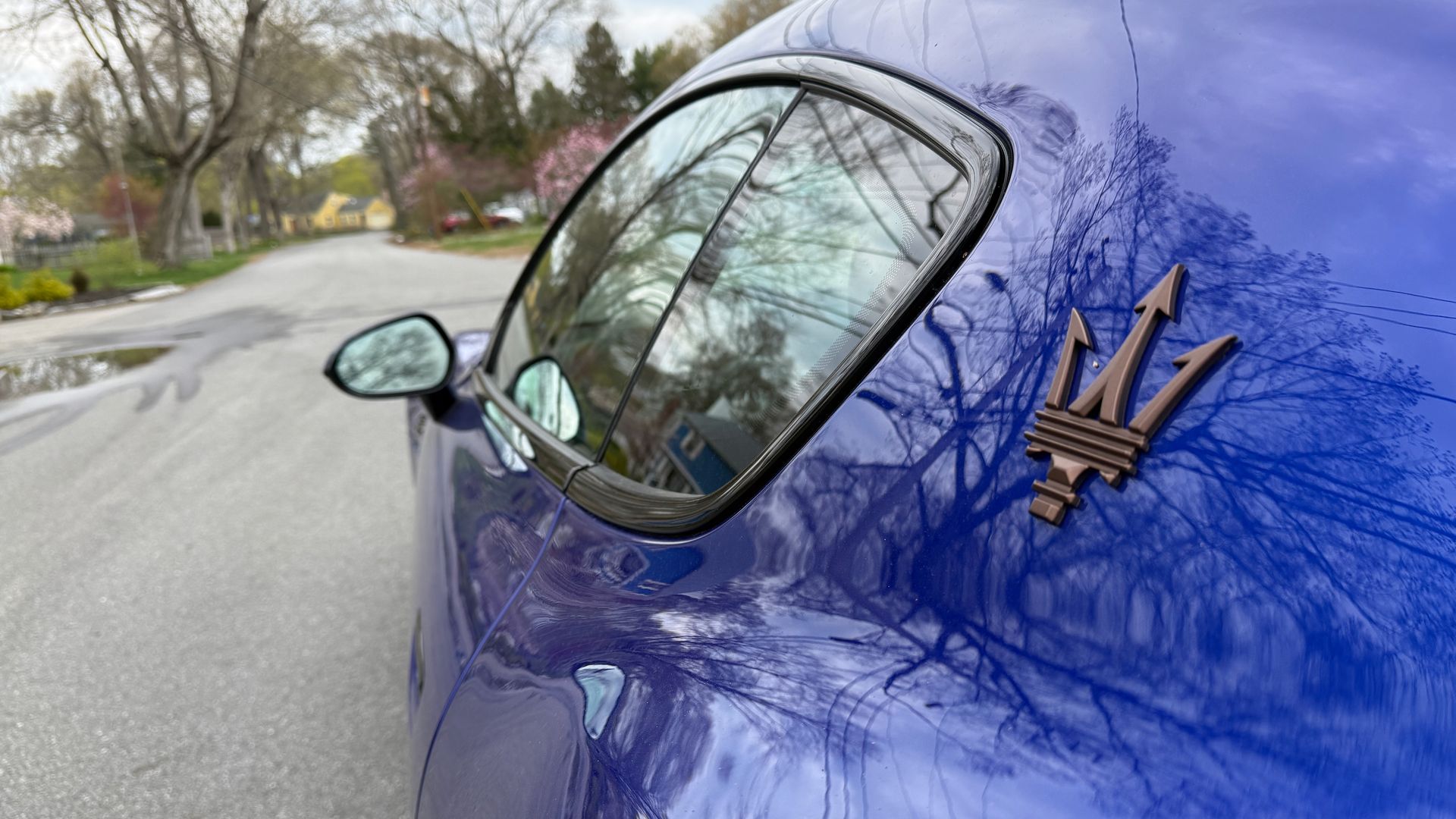A close-up of the Maserati logo on the bright blue exterior of the Folgore GranTurismo.