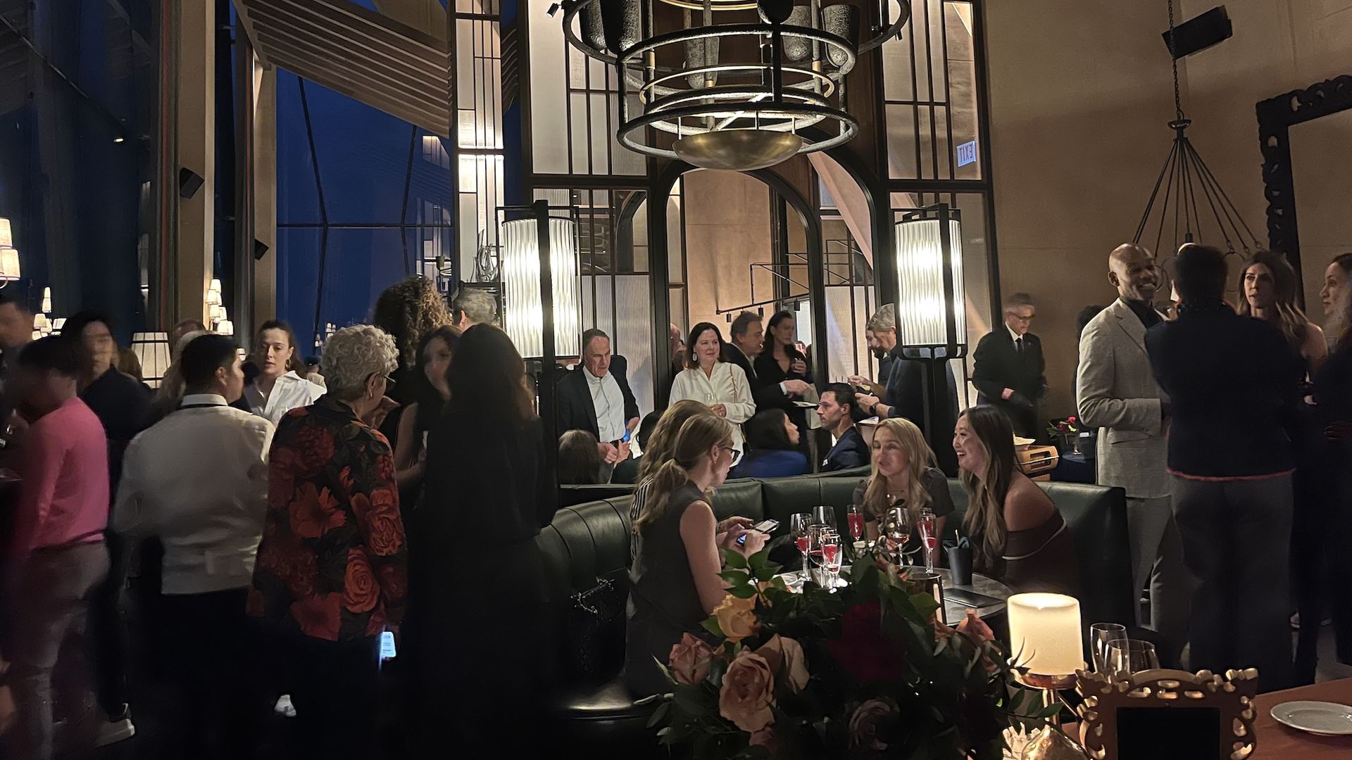 People standing around a restaurant and four women seated at a booth.