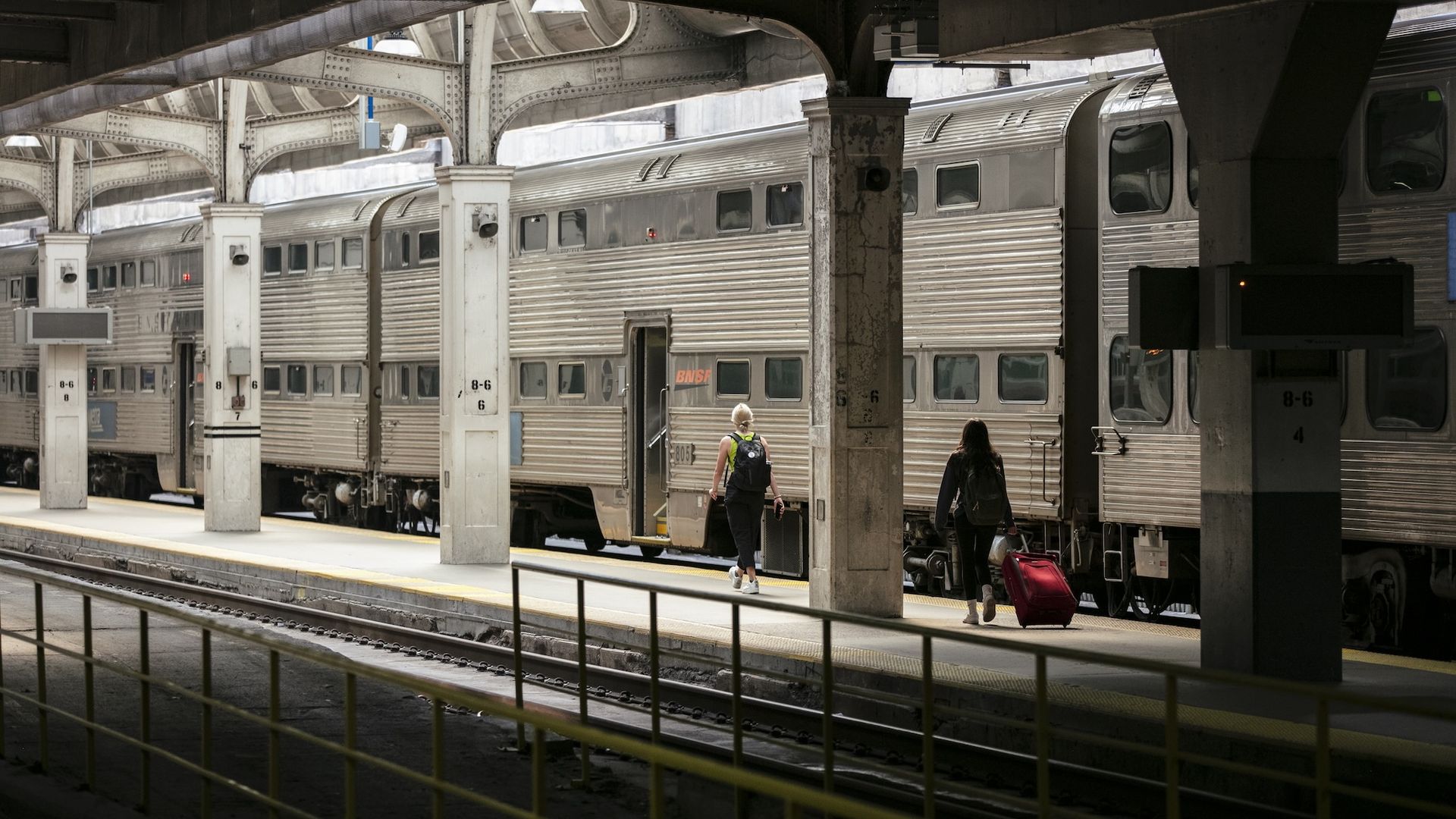 A Metra train at a station with two people walking up to the train.