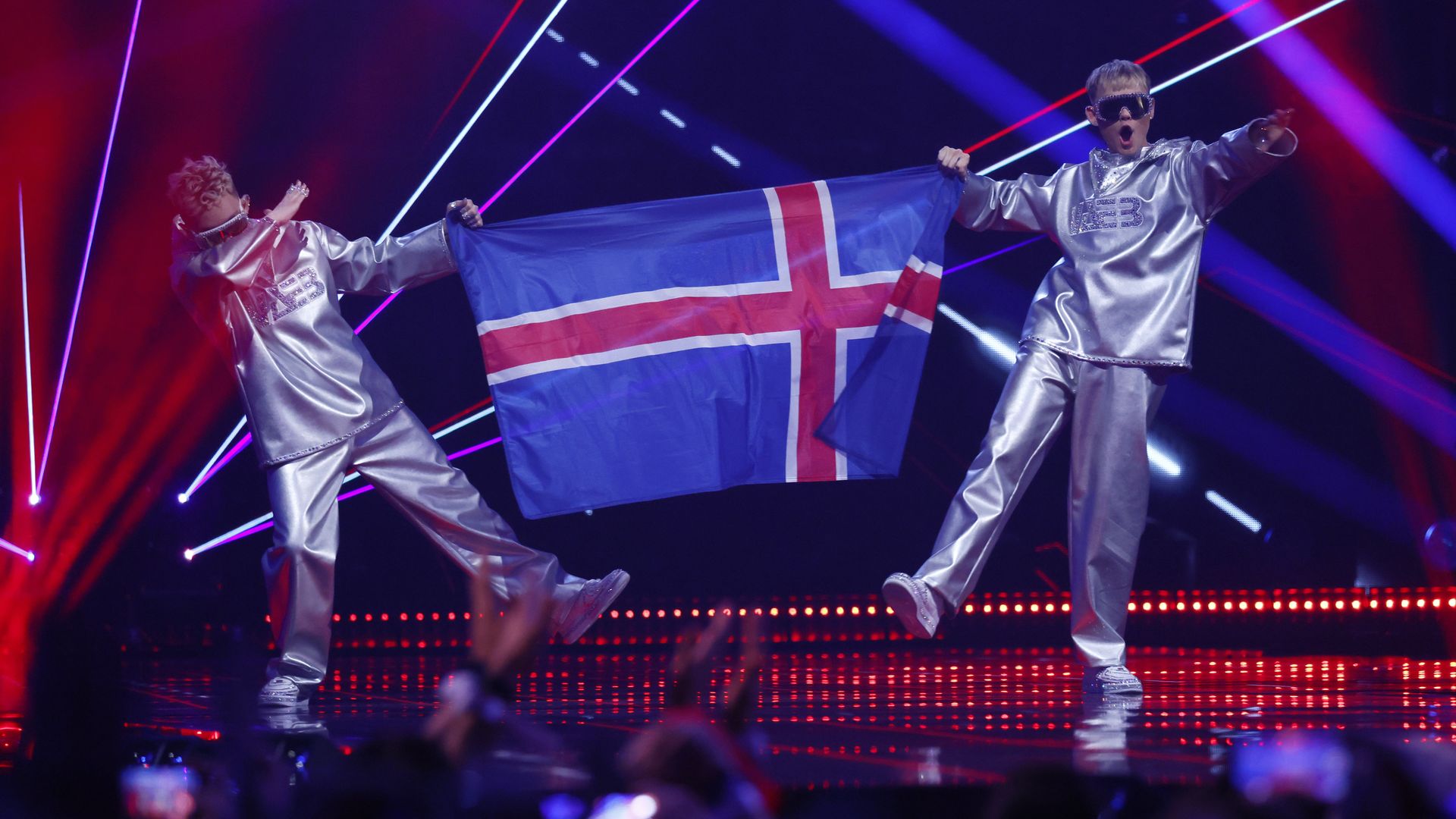VÆB, representing Iceland, walk on stage holding the national flag, featuring a red cross with a white outline on a blue background, during the Grand Final of the 69th Eurovision Song Contest.