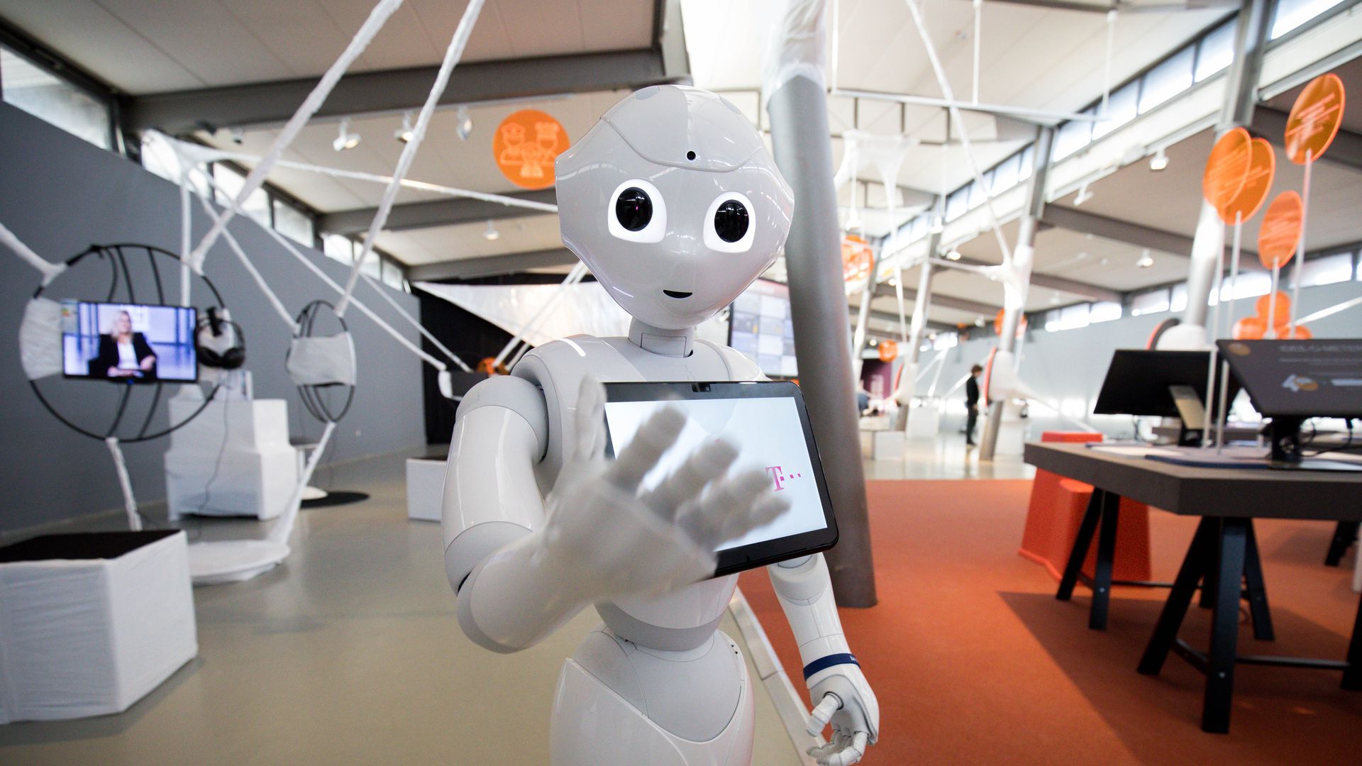 A humanoid robot gestures toward the camera.