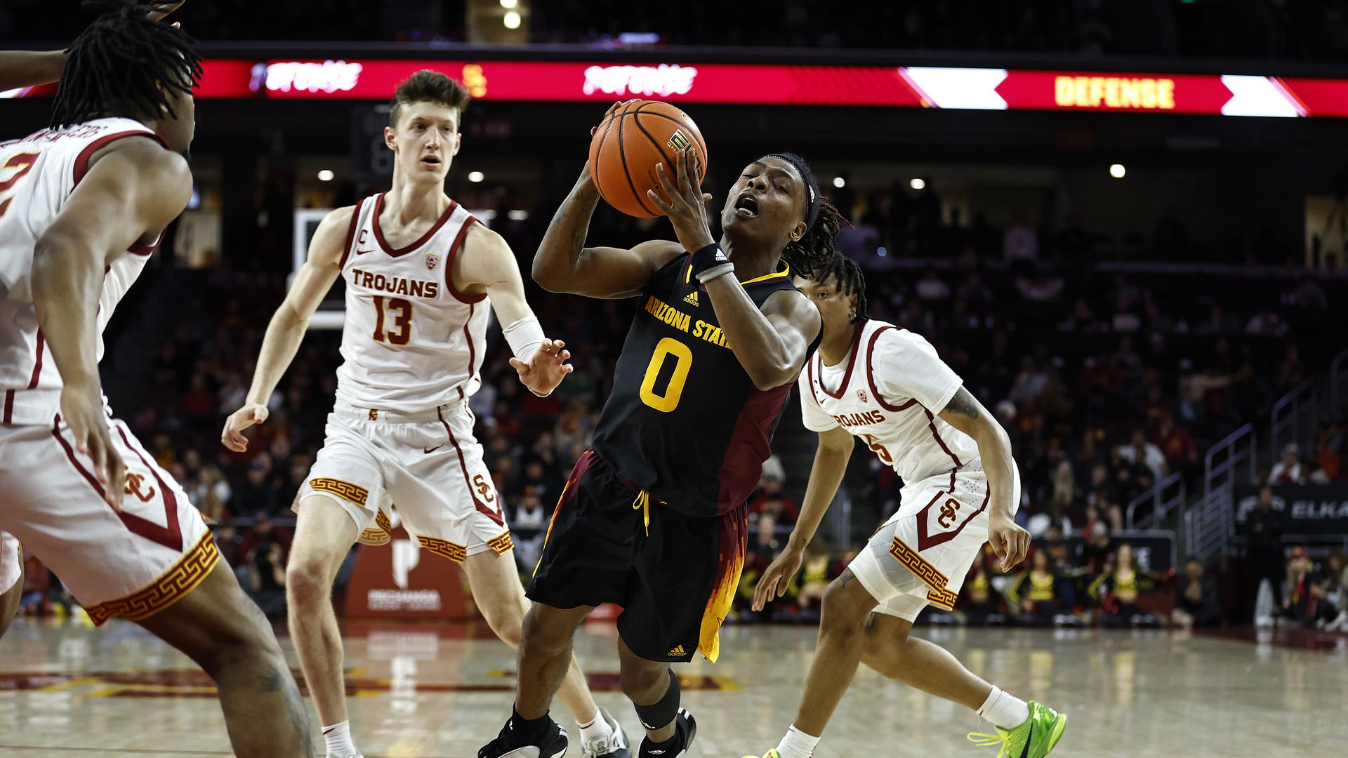 A basketball player surrounded by opponents falls after being fouled while taking a shot. 