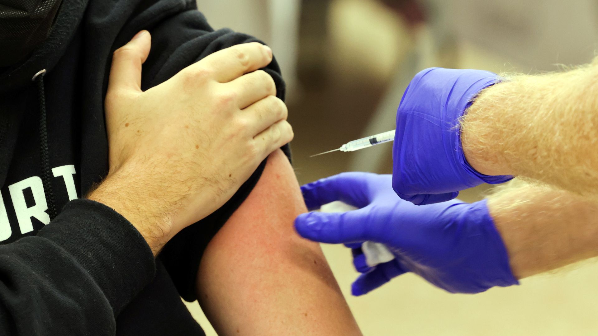 Photo of gloved hands reaching for an arm as a vaccine shot is about to be delivered