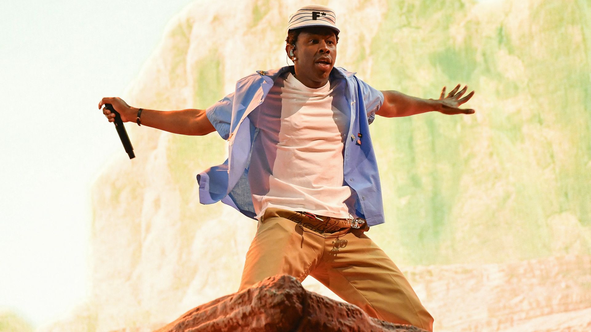 Photo of Tyler the Creator kneeling on stage with his hands flailed behind him as he performs