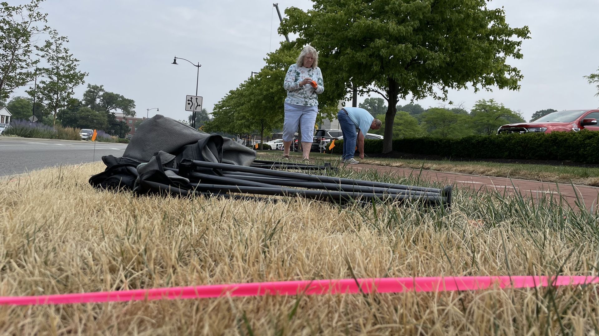 Chairs sit on the ground inside red tape as two people plant small flags to mark space along Rangeline Road in Carmel.