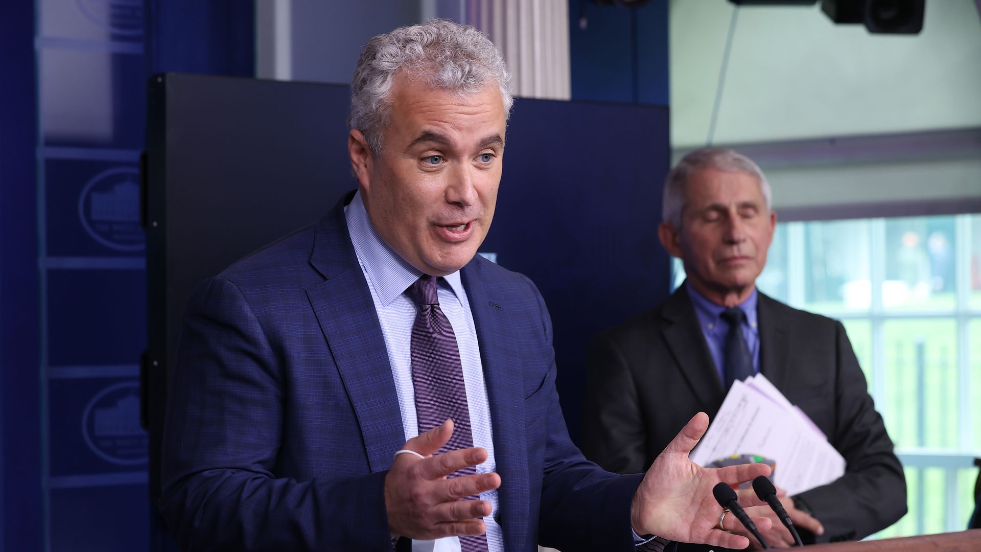 Photo of Jeff Zients speaking while gesturing with his hands, and Anthony Fauci standing behind him