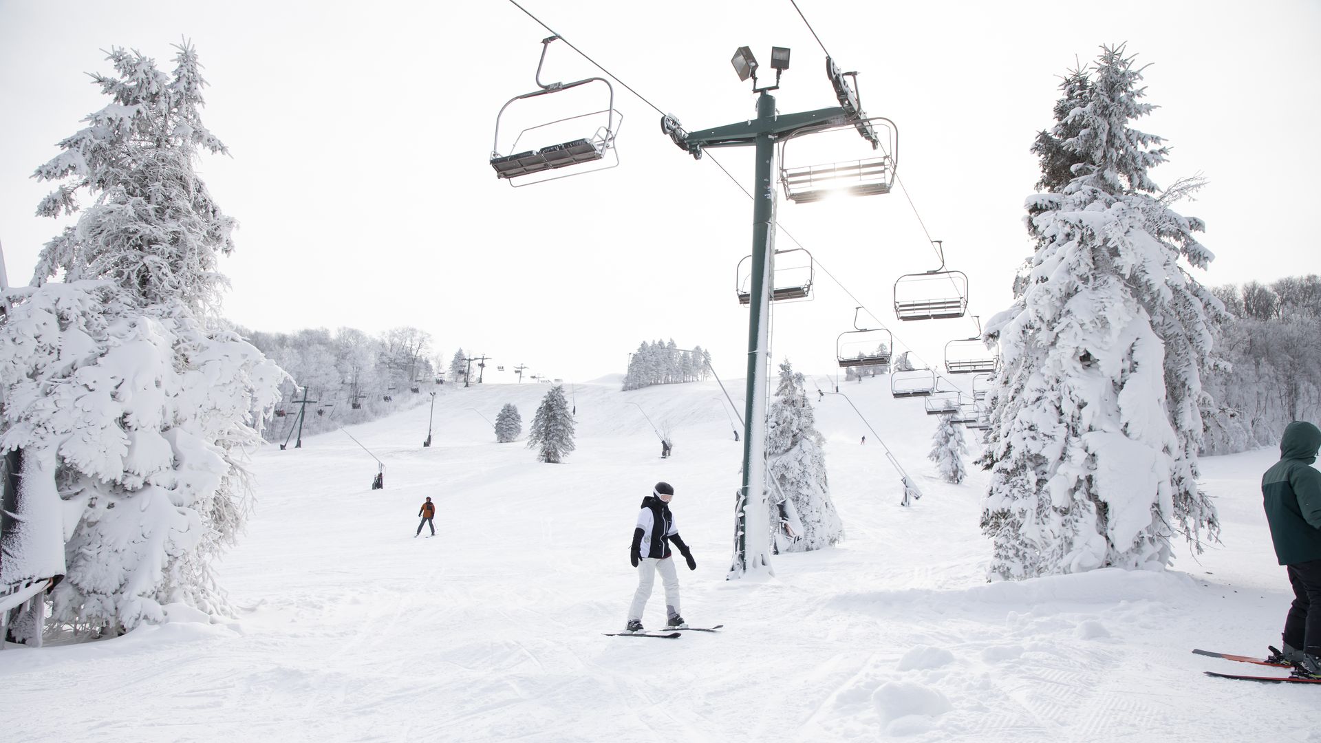 Skiers stand under a ski lift on a snowy mountain. 