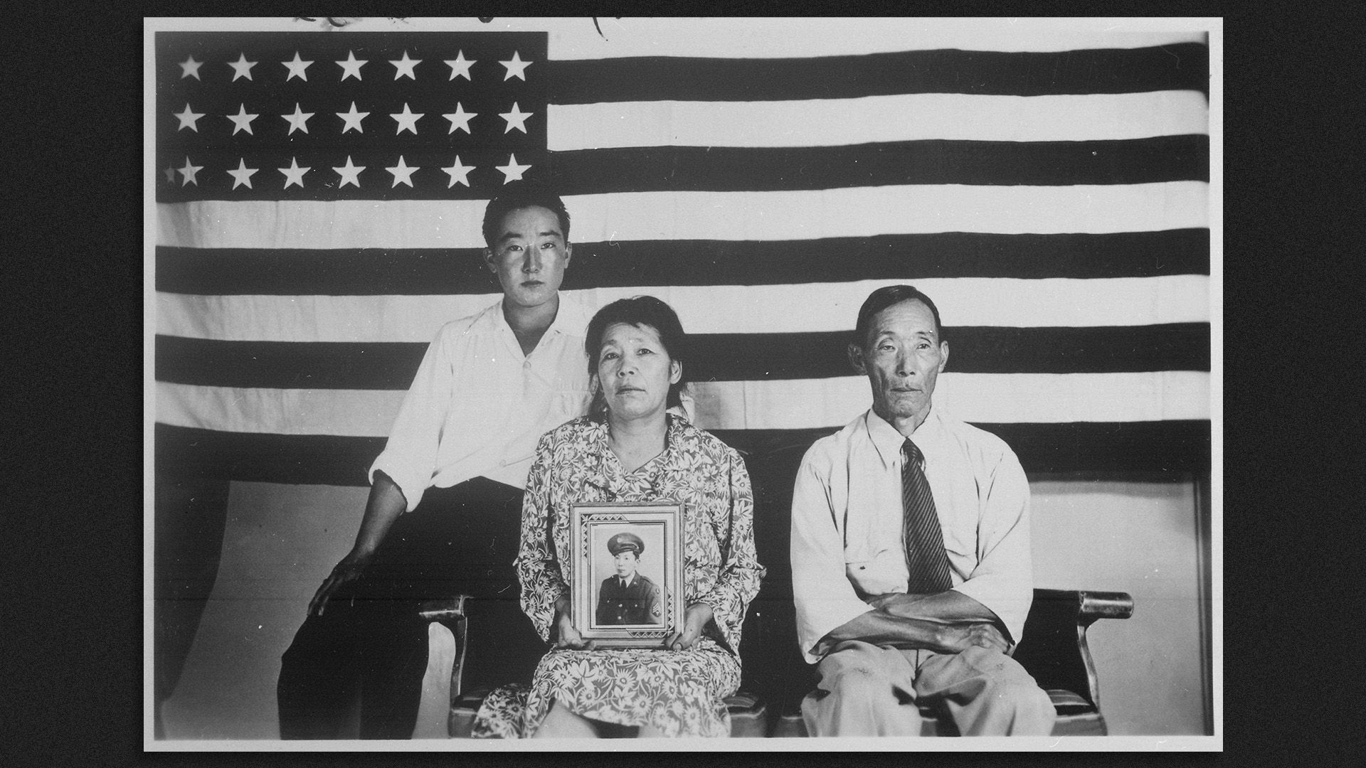 A family of three sits in front of the American flag