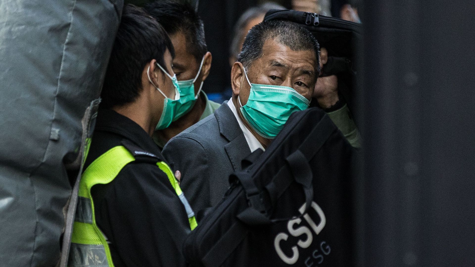 A short, dark graying haired Hong Kong media tycoon Jimmy Lai, wearing a green face mask, looks to his right as he's escorted into a Hong Kong Correctional Services van outside the Court of Final Appeal in Hong Kong on February 1, 2021.