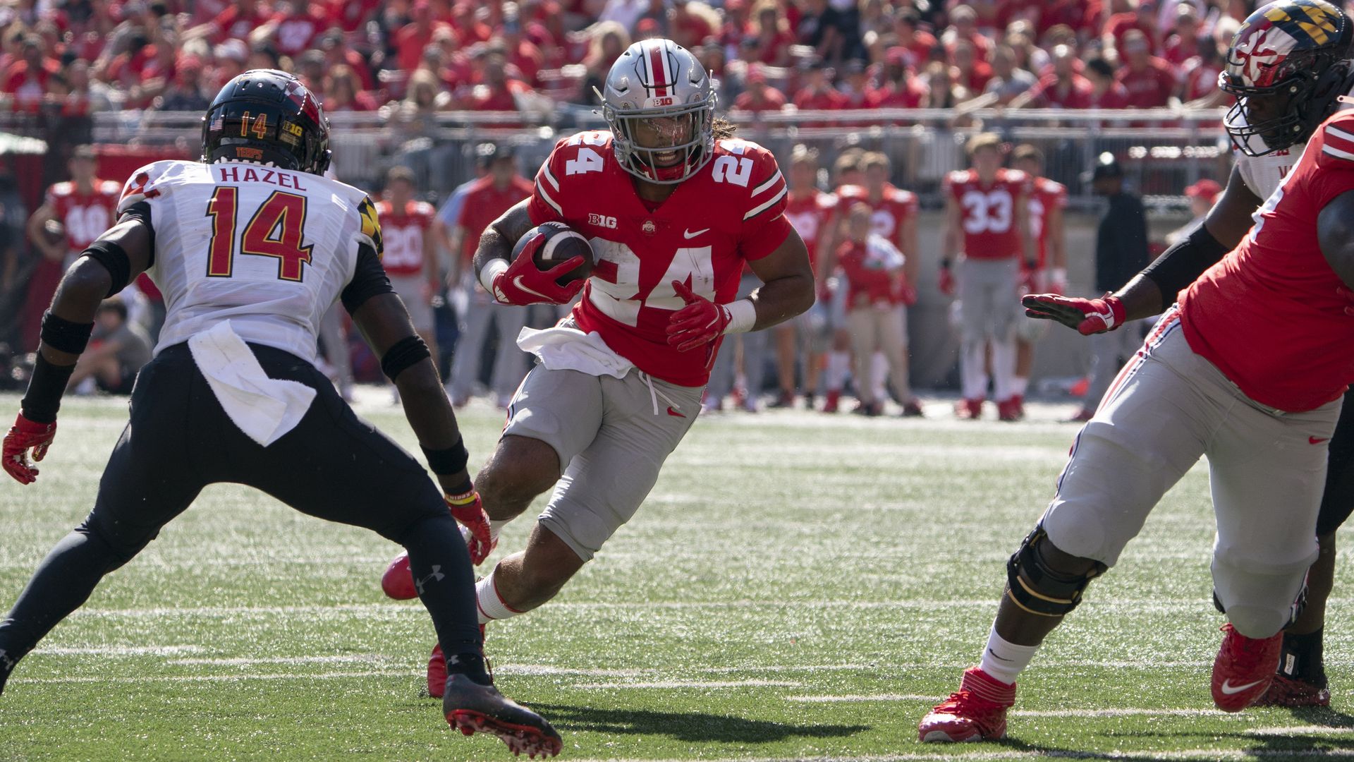 An Ohio State football player runs with the ball while evading an opponent from Maryland