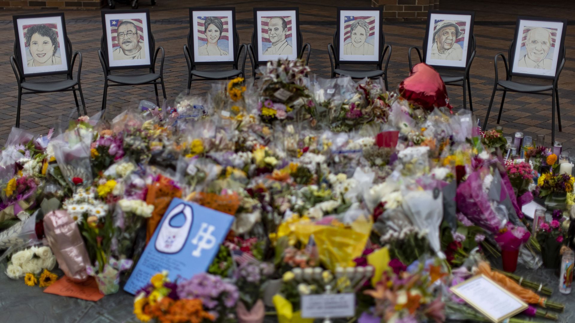 Photo of flowers laid on the ground in front of seven photographs of people 