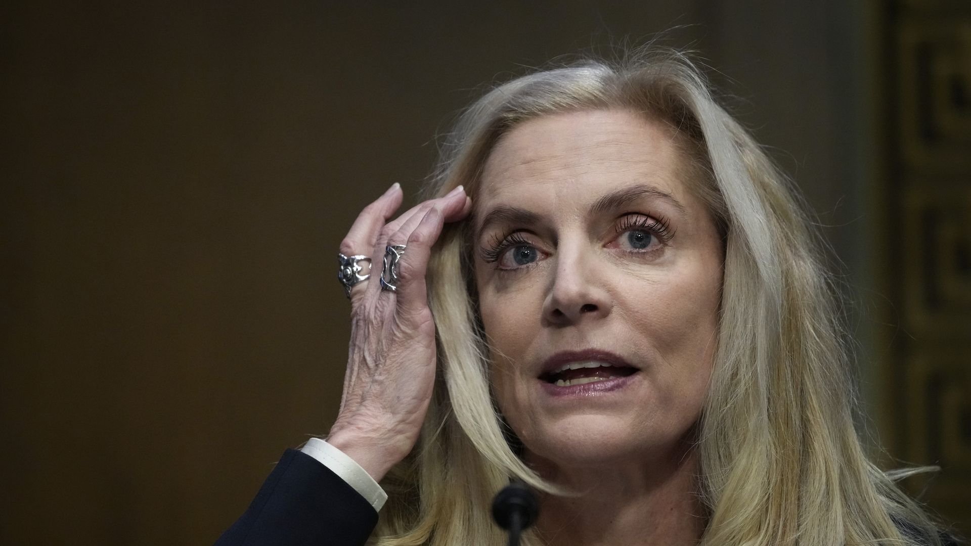 Lael Brainard moves her blond hair off the right side of her face with her right hand. Her mouth is slightly open
