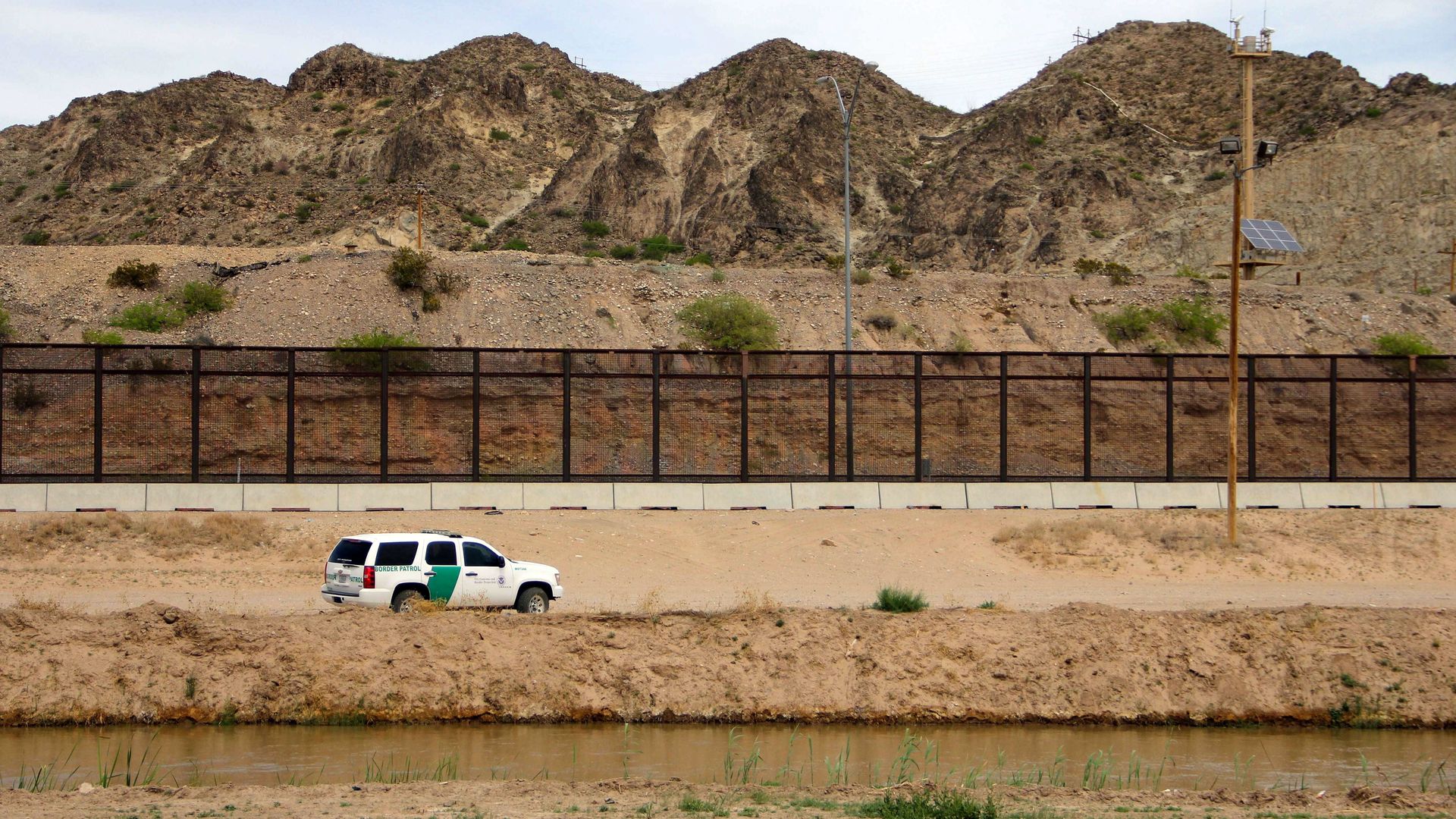 In this image, a border patrol car is parked along chain link fence at the U.S.-Mexico border.