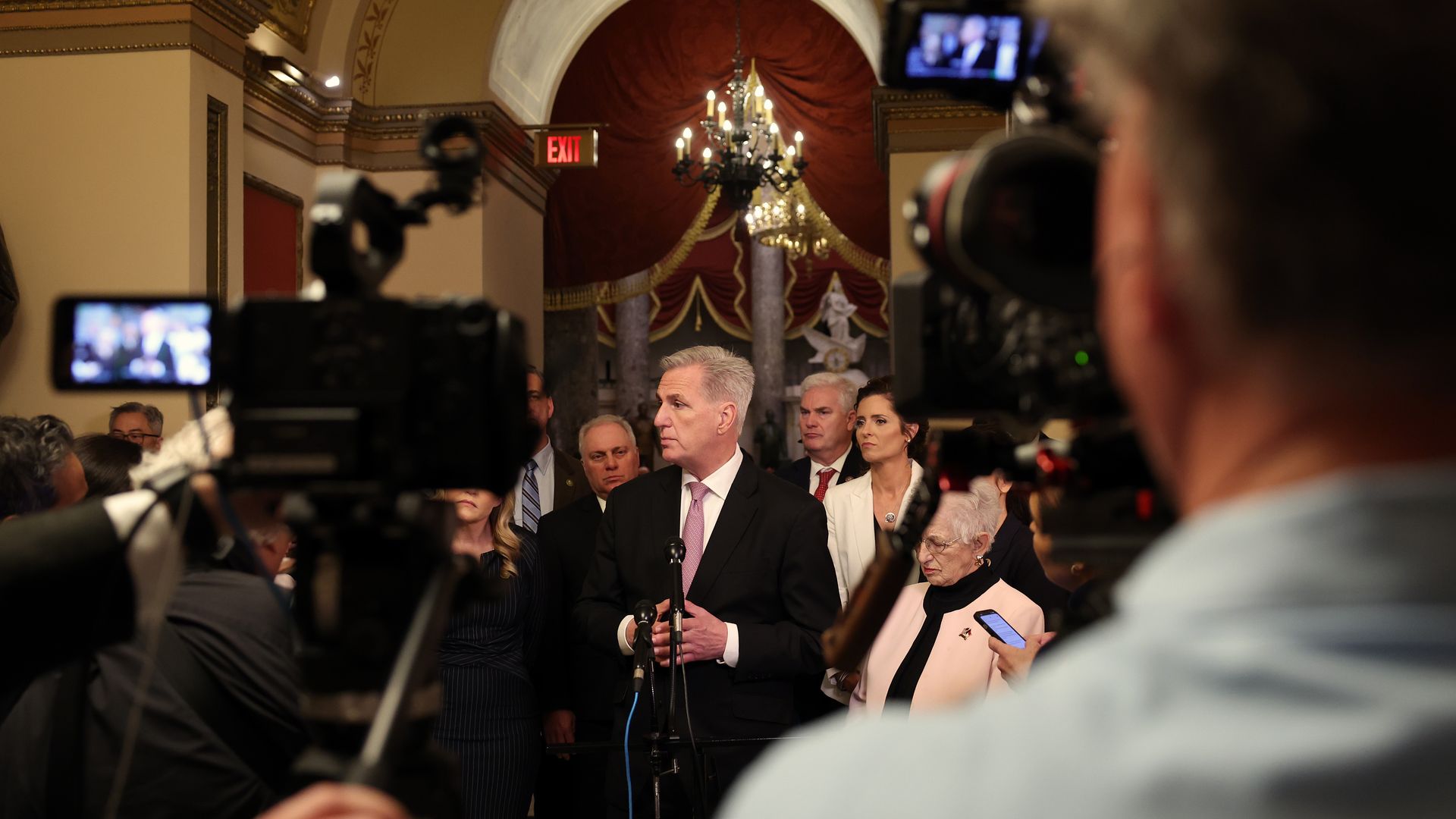 House Speaker Kevin McCarthy, wearing a dark gray suit, white shirt and pink tie, speaks to reporters in the Capitol along with other House Republicans.