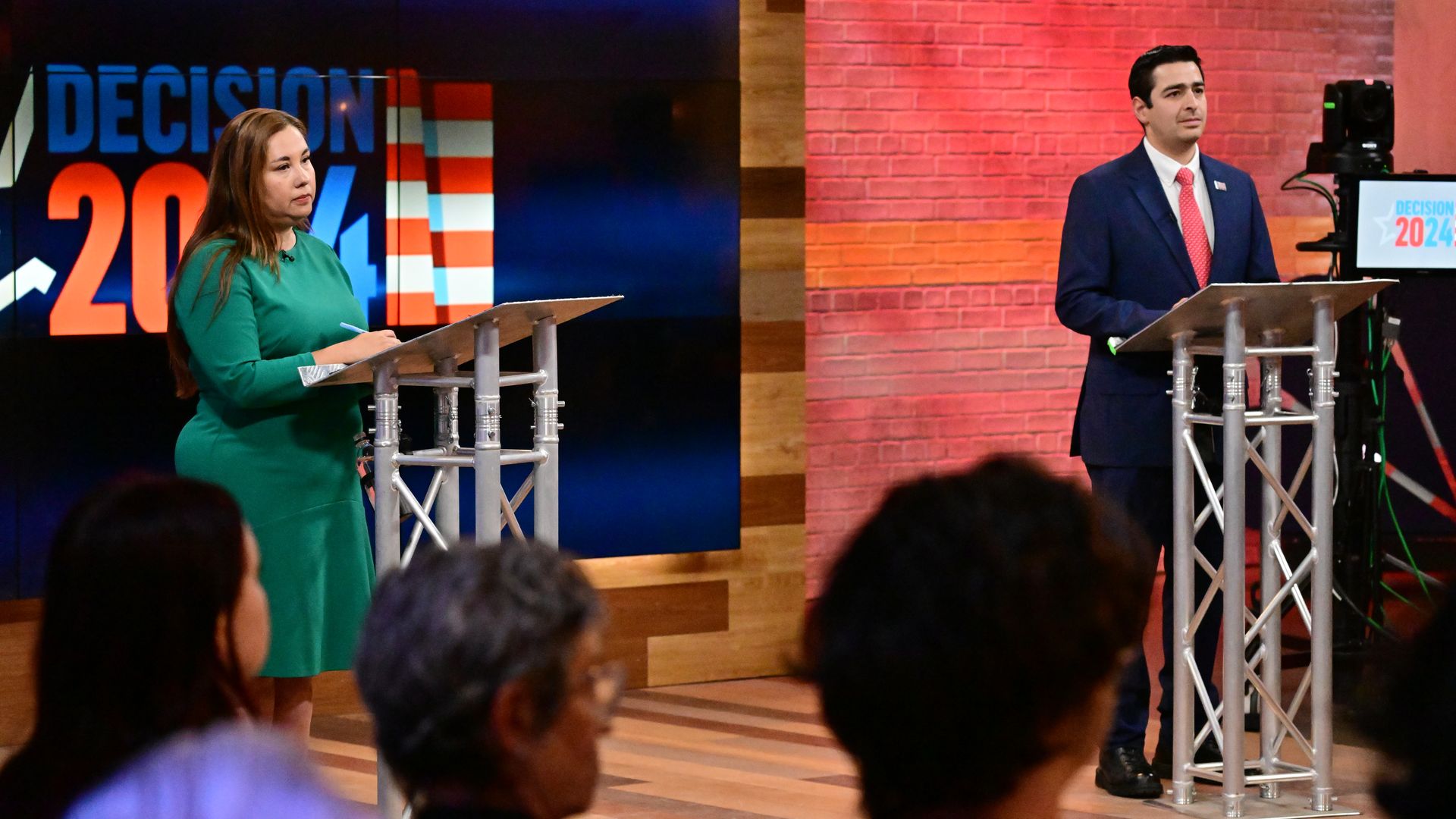 A woman in a green dresses stands on lectern while a man in a suit and tie stands near a lectern across from her. 
