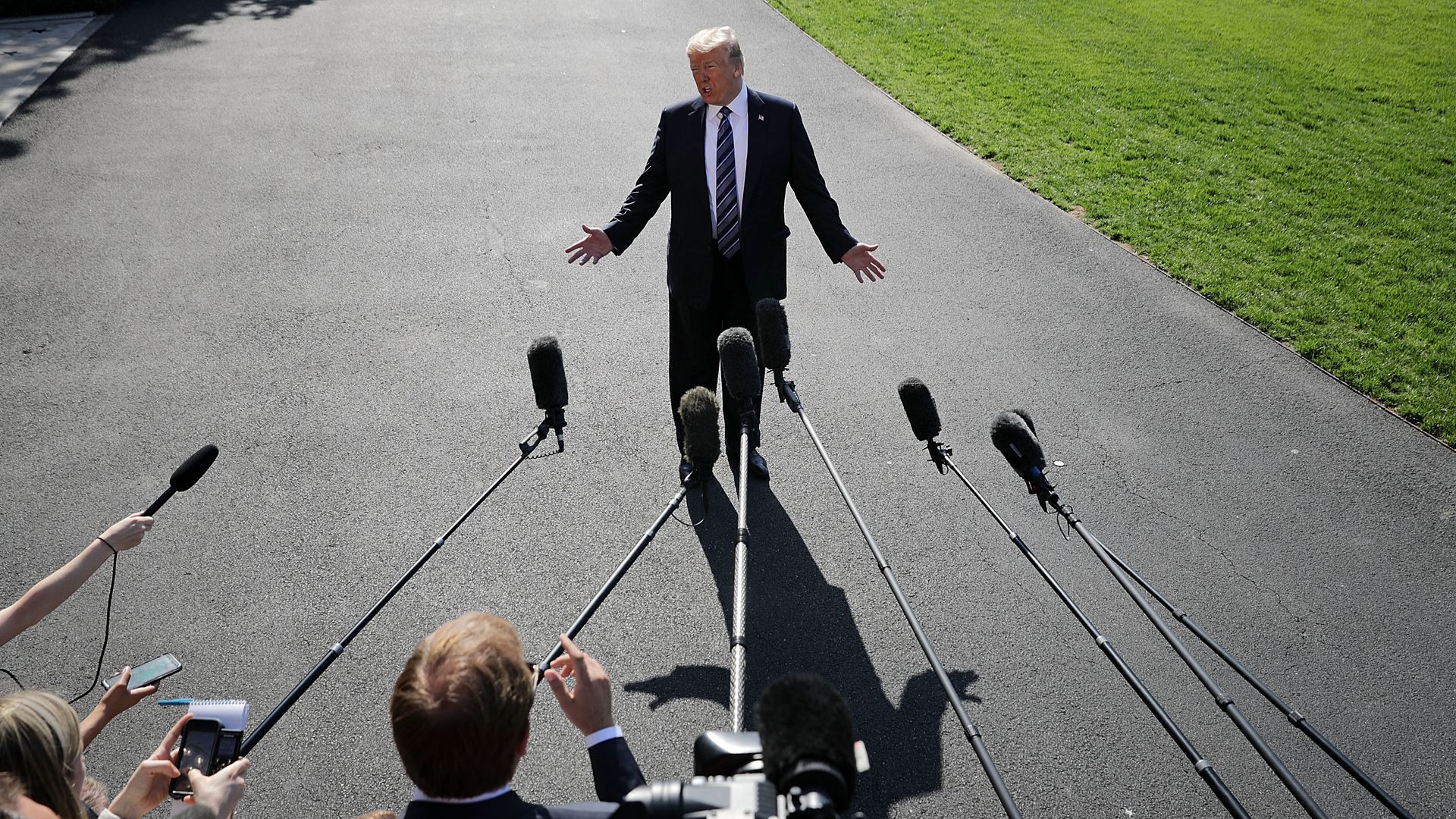 Donald Trump standing on asphalt surrounded by microphones.