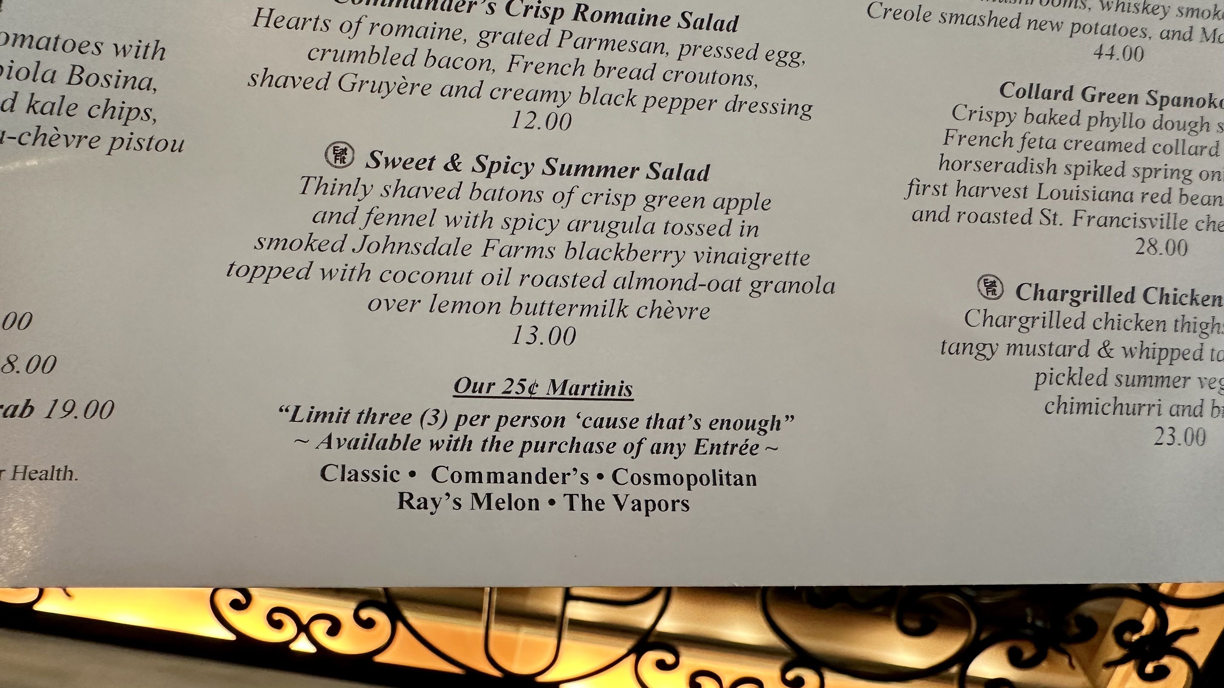 Close-up of a restaurant menu page in elegant serif type. Center item: "Sweet & Spicy Summer Salad" with apple, fennel, arugula, blackberry vinaigrette, almond-oat granola over lemon chèvre; 13.00.