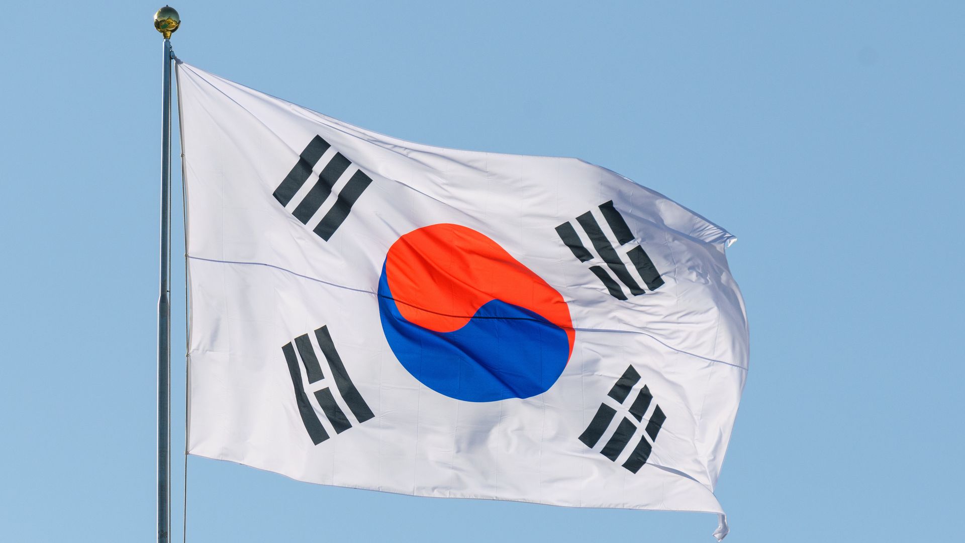 The white flag of South Korea waving on a flagpole against a clear blue sky.