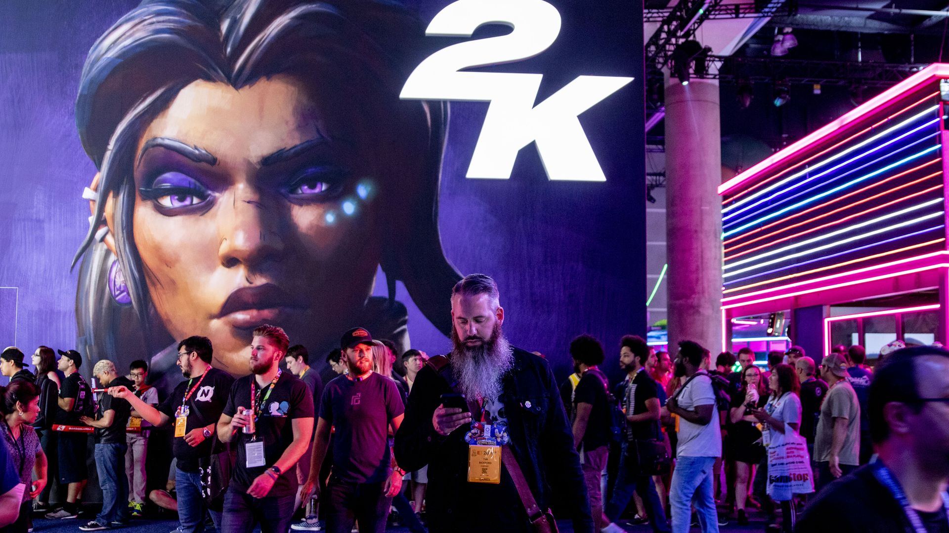 Photo of people standing in a darkened conference hall in front of a massive sign showing a woman's face and the logo for 2K Games