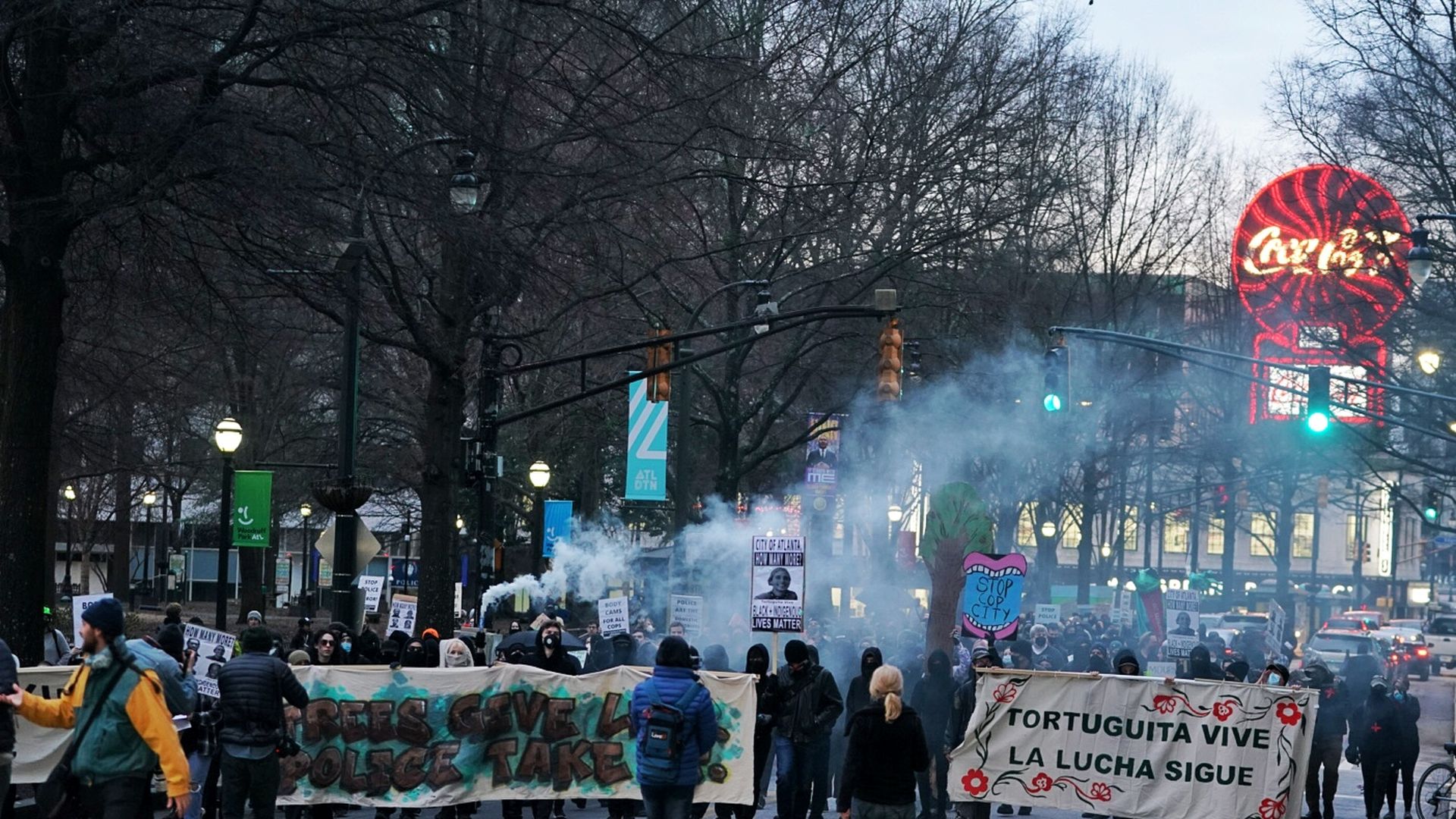 A crowd of people carrying banners march in the streets of Atlanta as smoke rises from the crowd