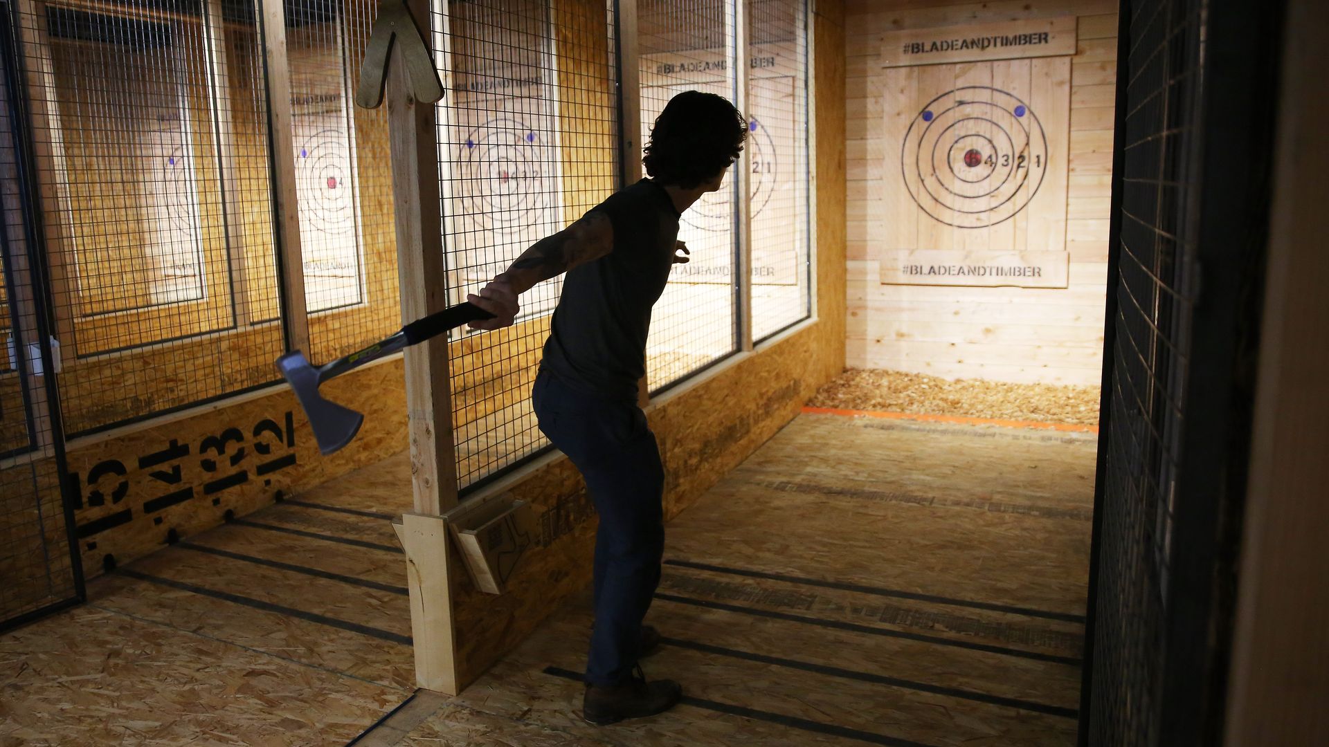 A person in silhouette preparing to throw an axe, in a lane closed in by wood and wire, with a wooden target in the distance.