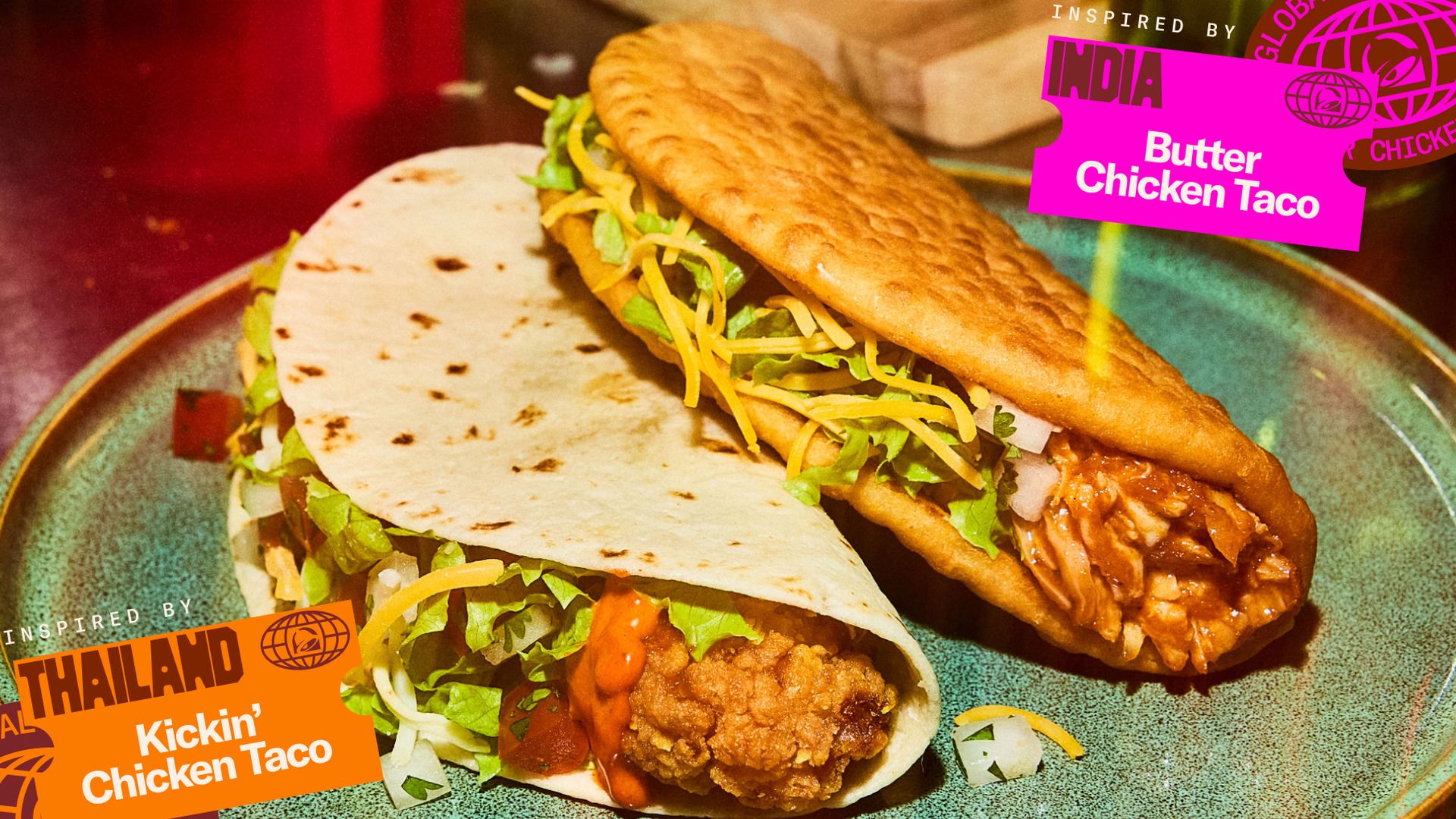 Two tacos on a teal plate: a fried chicken taco with lettuce and cheese, and a butter chicken taco with greens. Bright pink "Butter Chicken Taco" and orange "Kickin' Chicken Taco" labels adorn the scene.