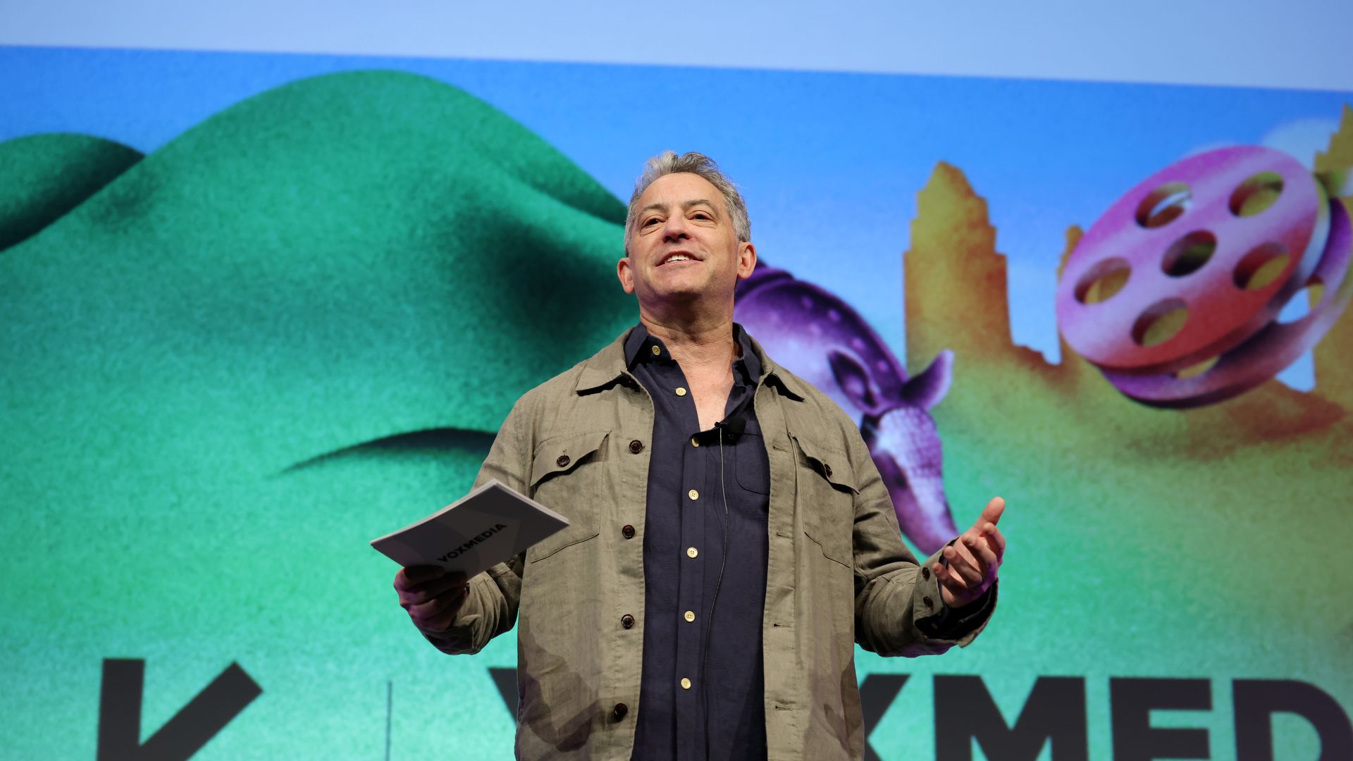 Vox Media CEO Jim Bankoff speaks onstage at an event wearing a olive green shirt over a navy blue button up shirt.