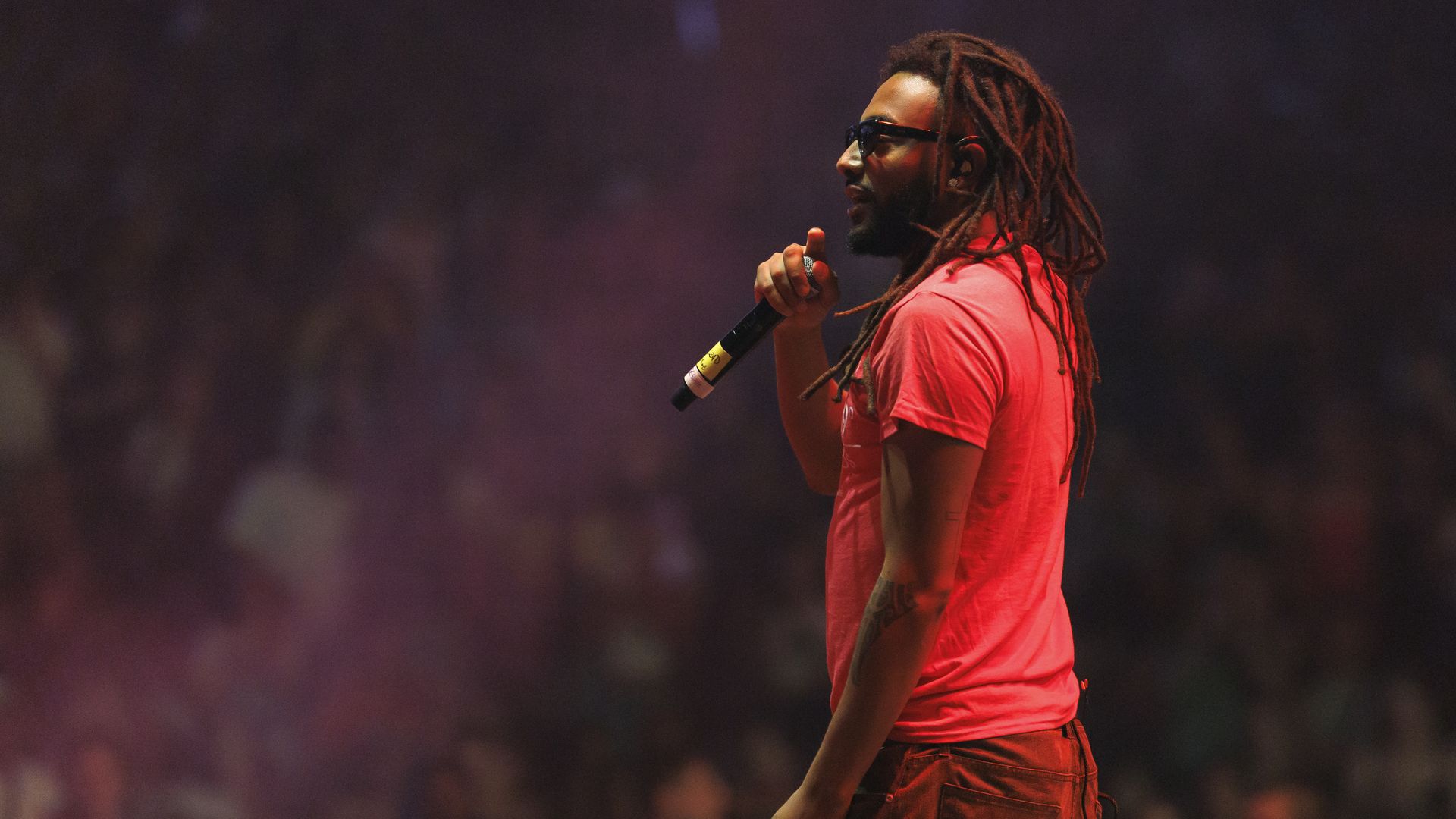 A photo of a person turned away from the camera, holding a microphone and facing a crowd.