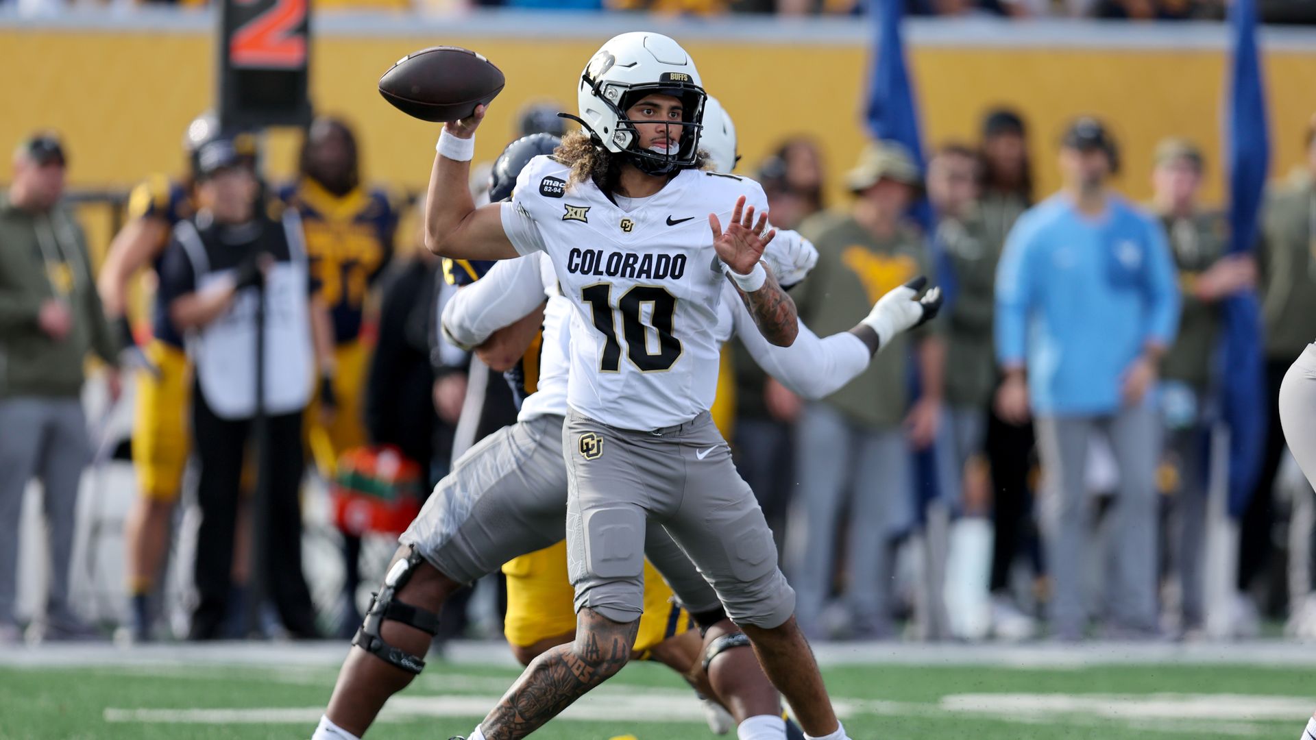 Julian Lewis  wearing white Colorado uniform number 10 preparing to throw a pass on the field during a game, with players and spectators blurred in the background.