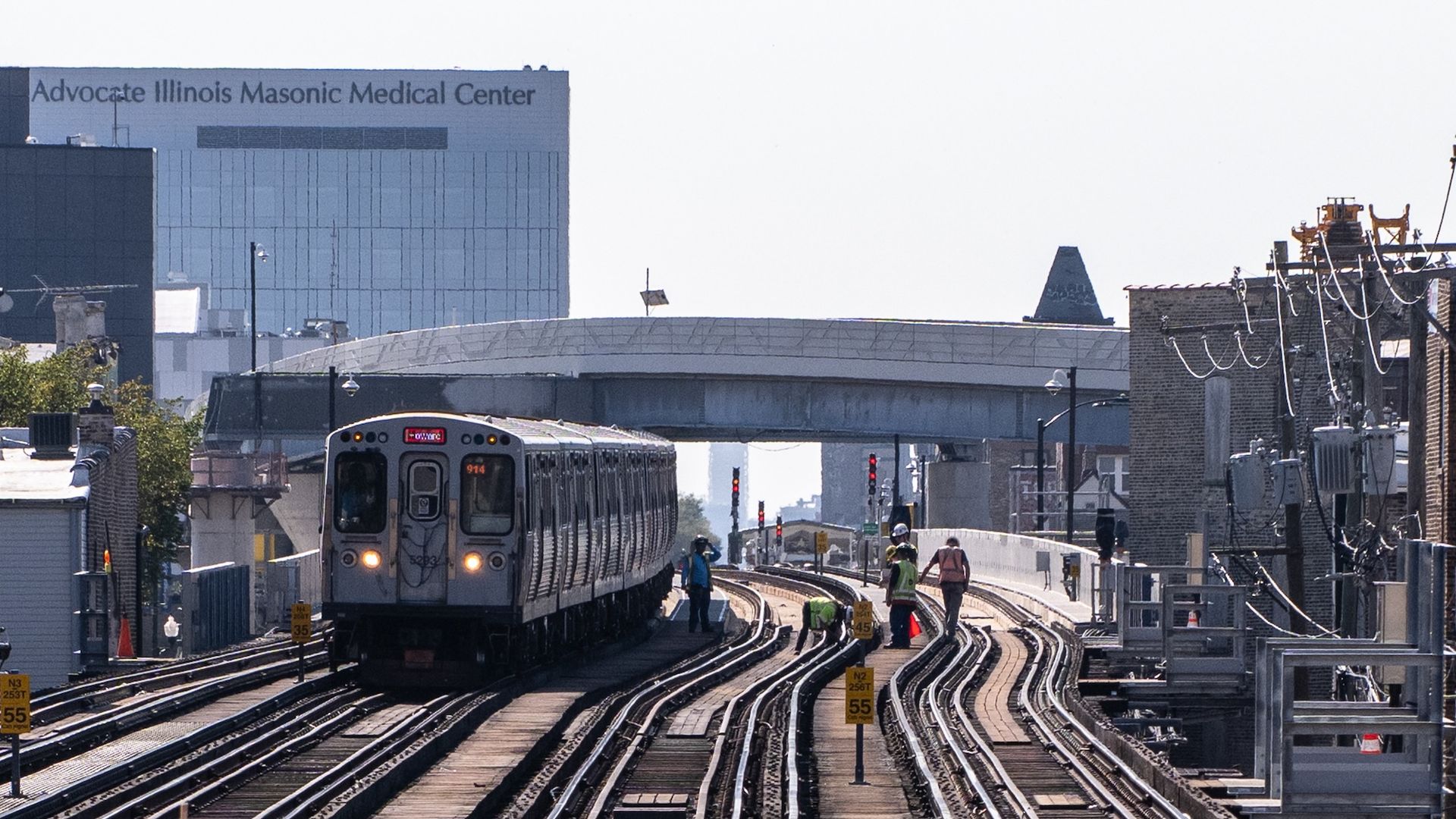 A CTA train approaching on a tracks with an overpass and hospital behind it.
