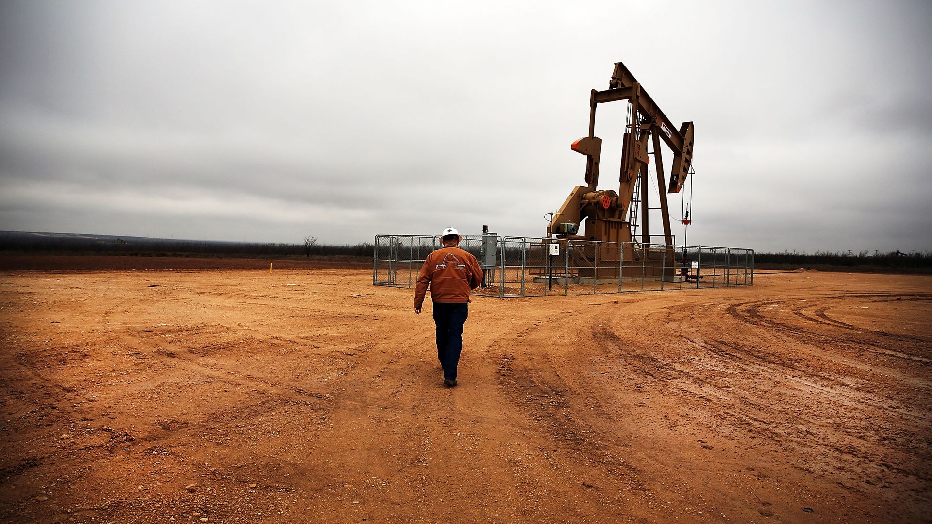A man walks towards an oil well alone. 
