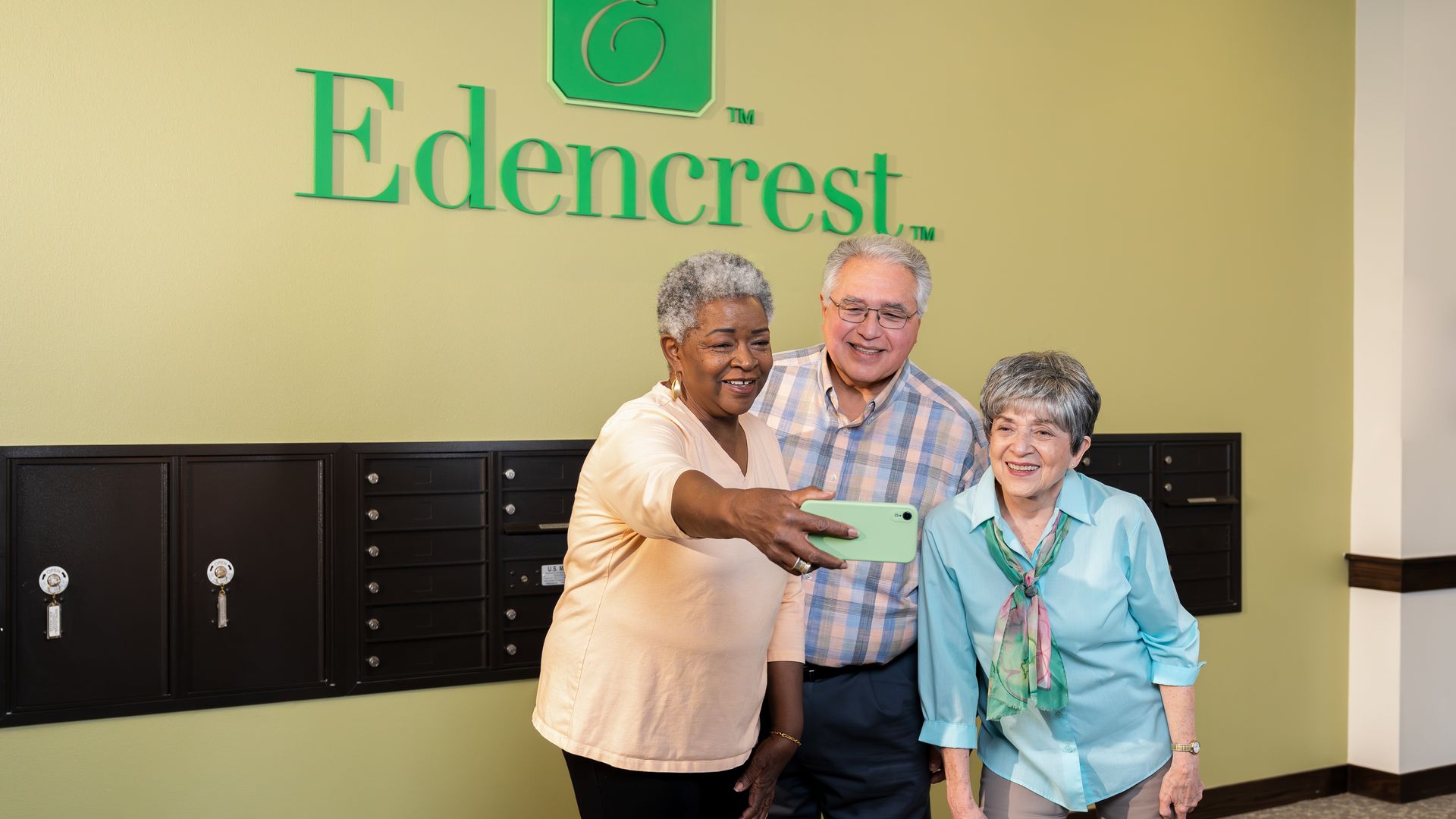 Three seniors stand in front of an "Edencrest" sign, posing for a selfie.