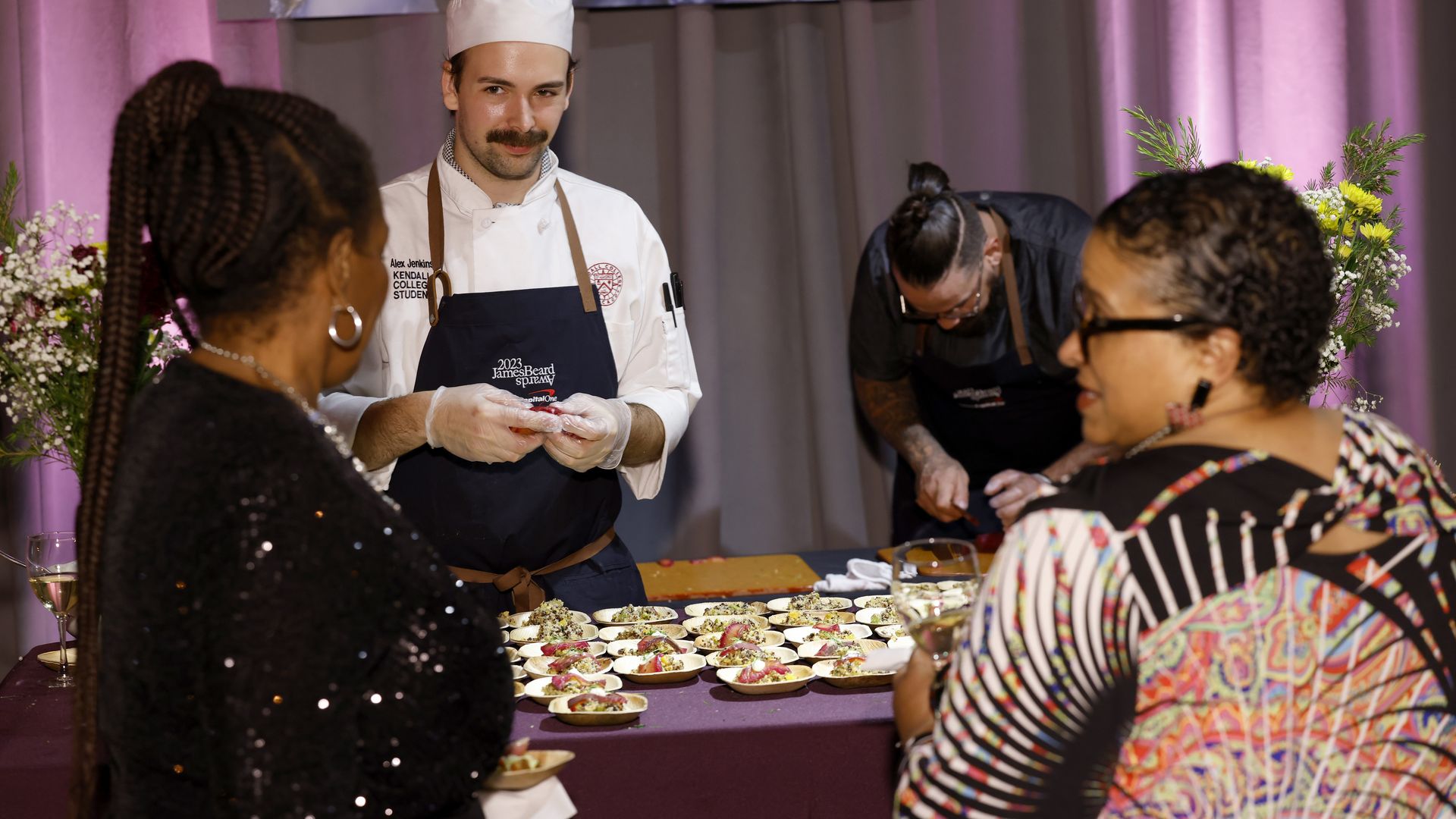 Photo of guests standing at a table of hor d'oeuvres while they speak with a worker