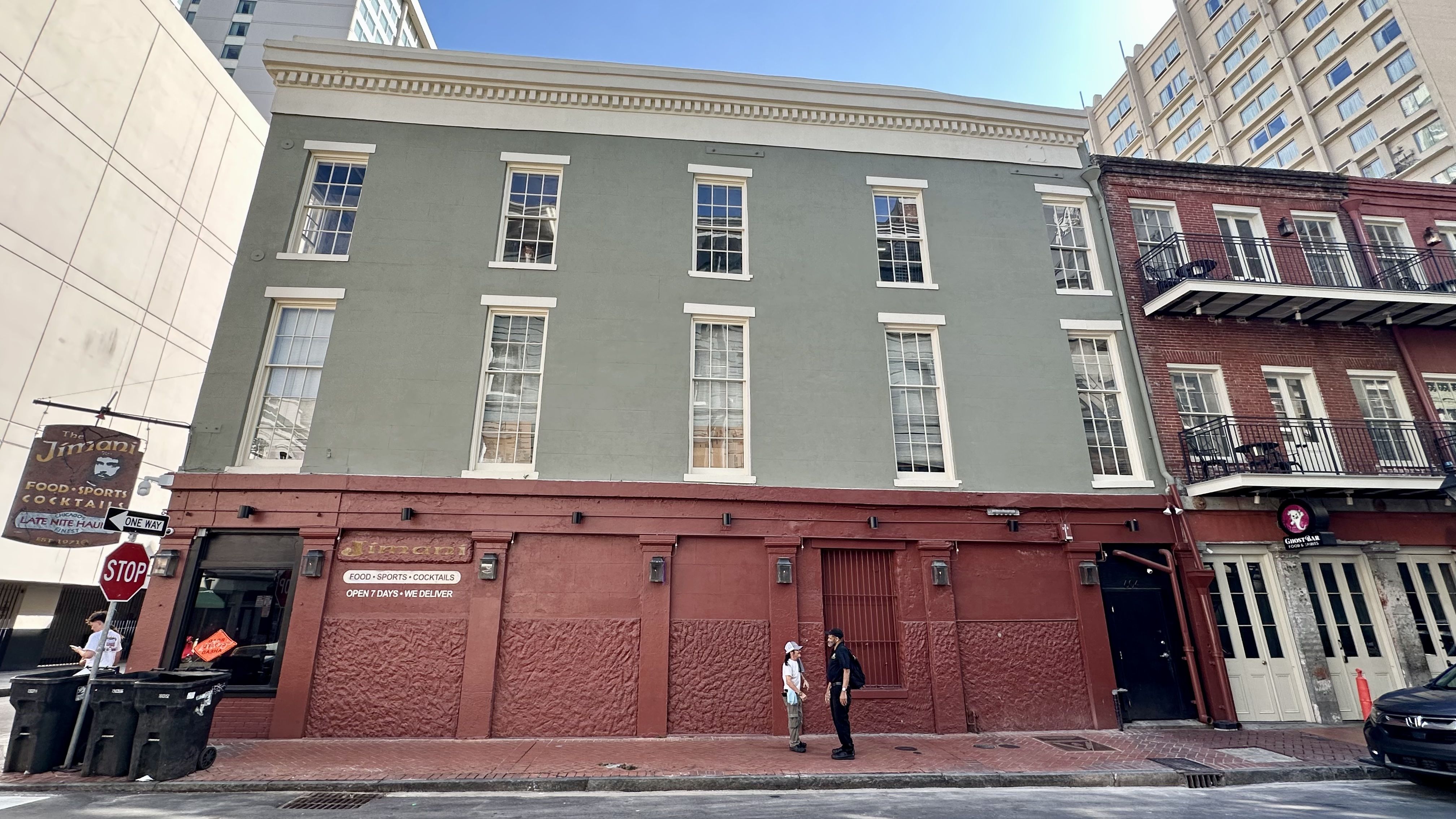 Image shows a green and brick building in the French Quarter with people on the sidewalk.