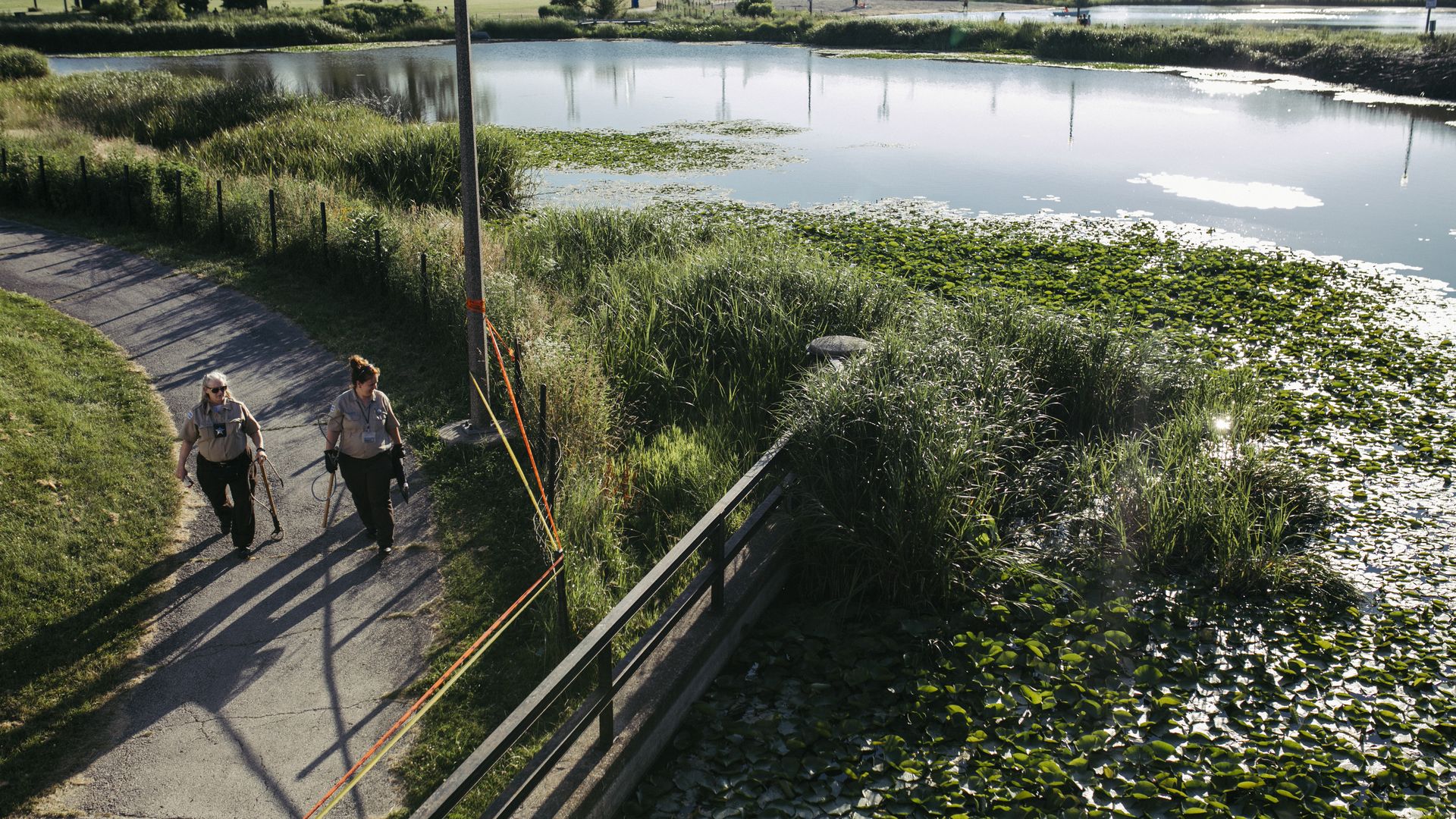 Photo of two people walking on a park trail in front of a lagoon.