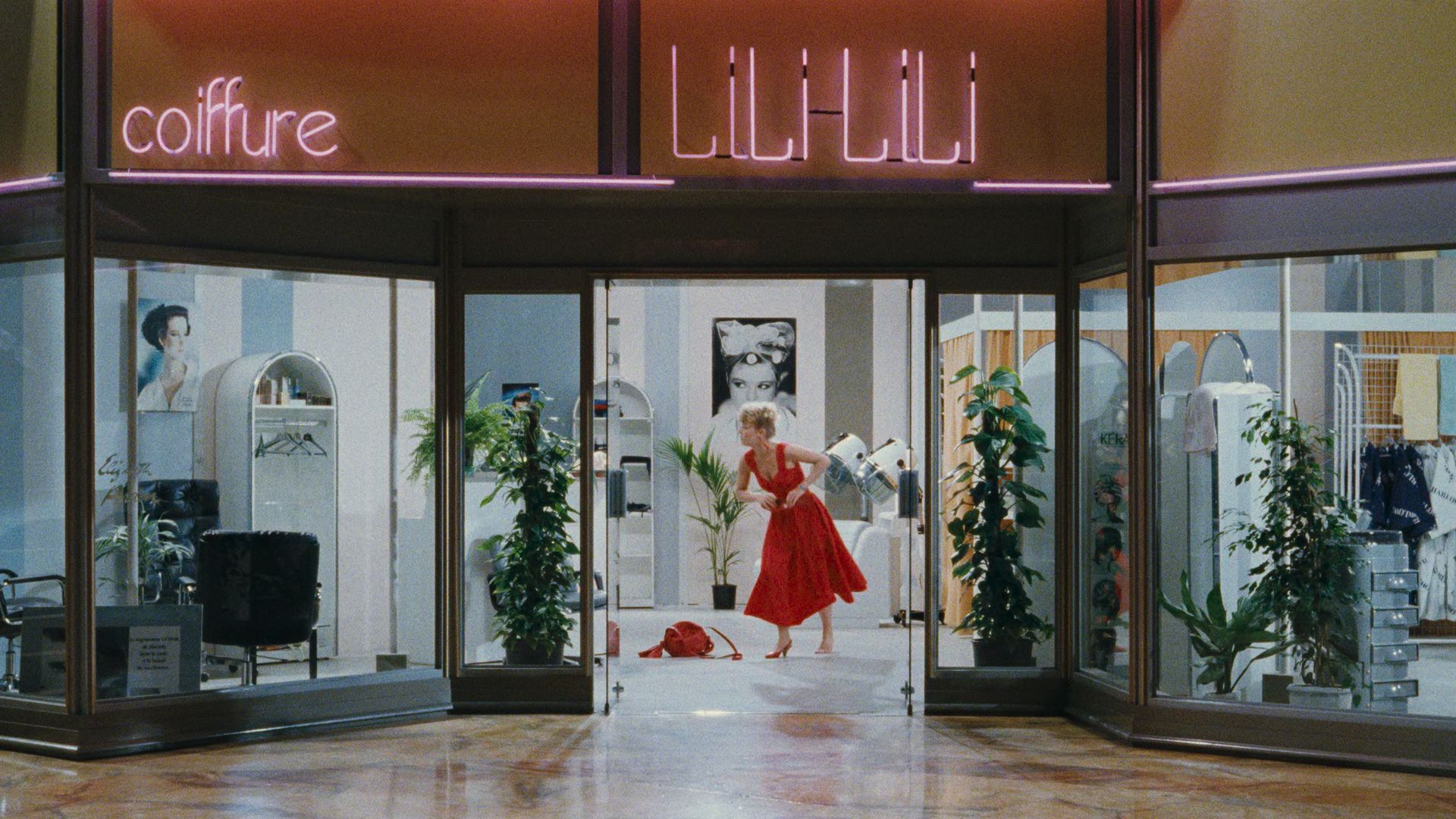 A still from the film "Golden Eighties" centered on a woman in a red dress at a department store. 