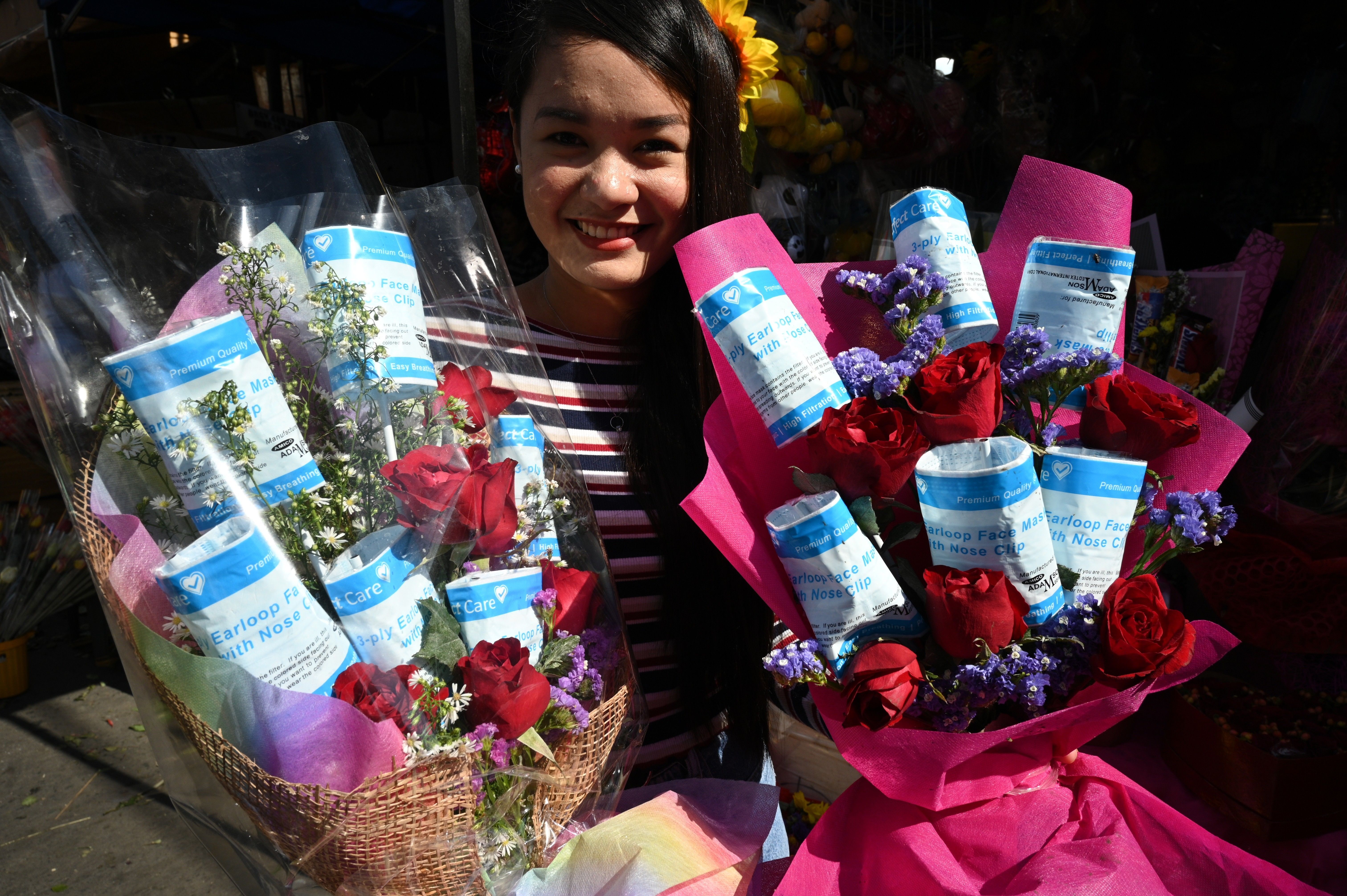 In this image, a woman holds two bouquets of flowers and face masks. She is not wearing one